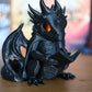 Figurina dragon negru cu ochi luminați portocaliu, citind o carte pe o masă din lemn, decor fantasy mistic pentru pasionații de cărți și povești cu dragoni.