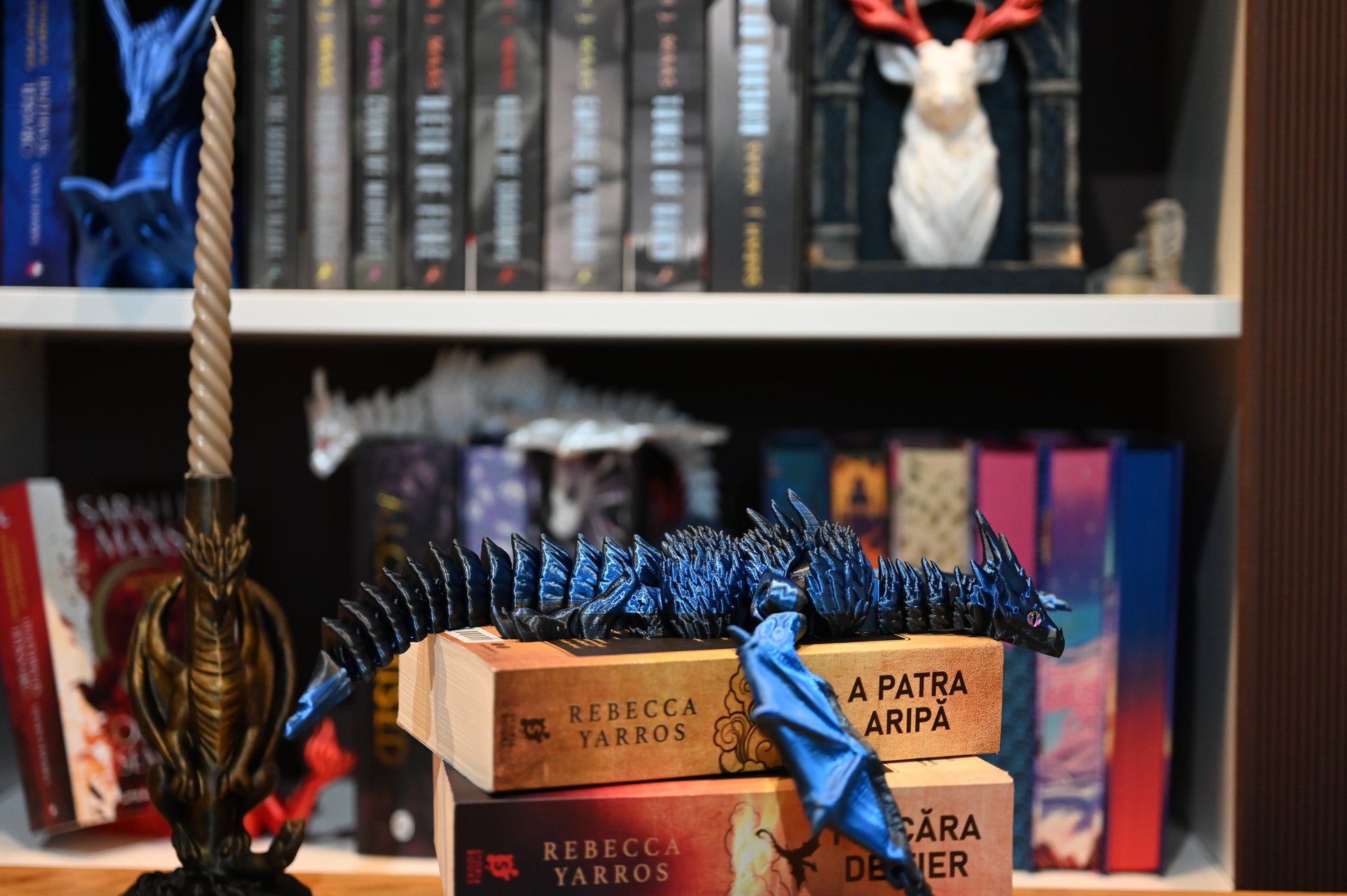 Figurina 3D articulată Dragon albastru articulat așezat pe romanele „A Patra Aripă” de Rebecca Yarros, decor perfect pentru pasionații de lectură și fantezie.