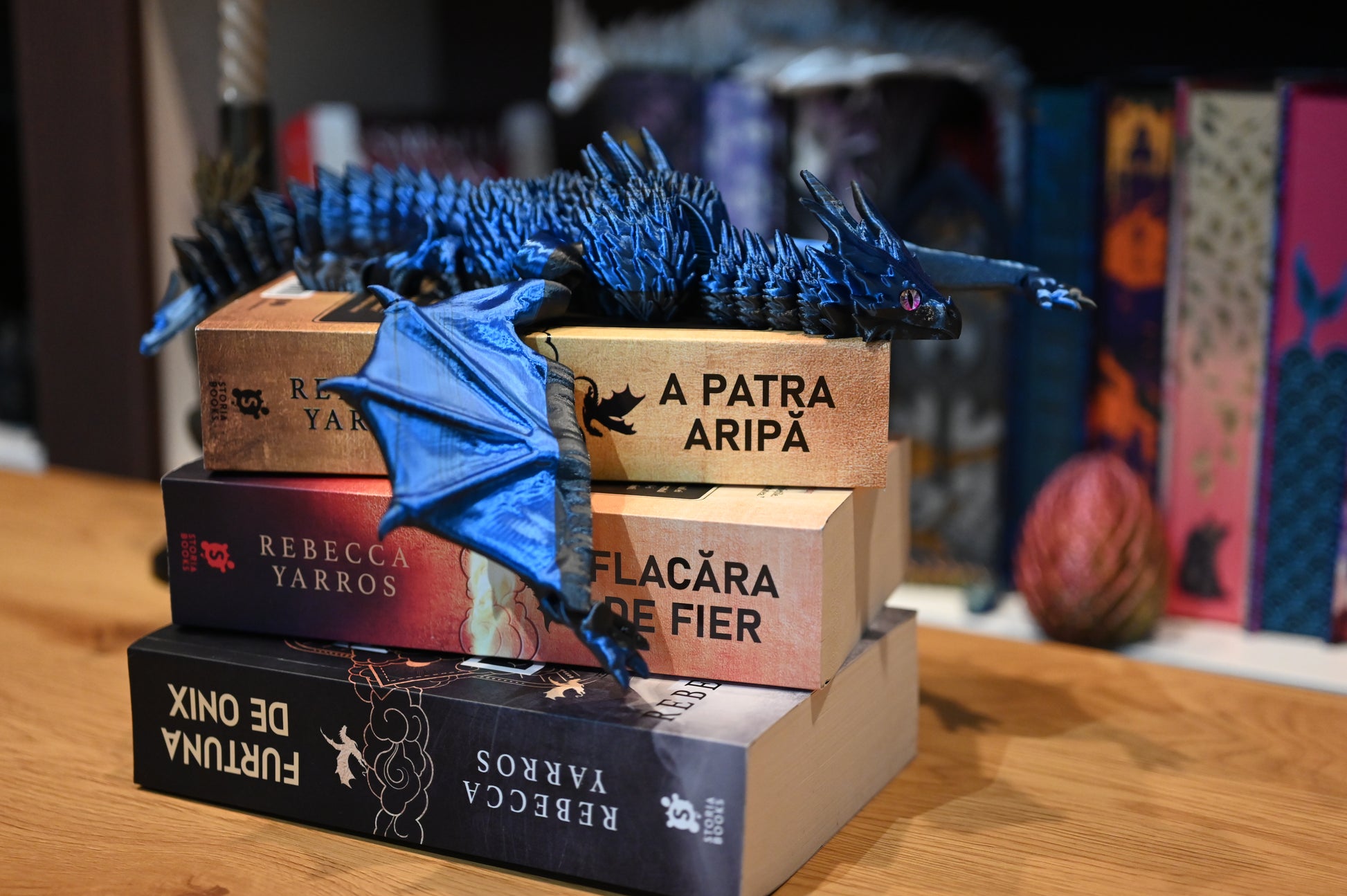 Figurina 3D articulată Dragon albastru articulat așezat pe romanele „A Patra Aripă” de Rebecca Yarros, decor perfect pentru pasionații de lectură și fantezie.