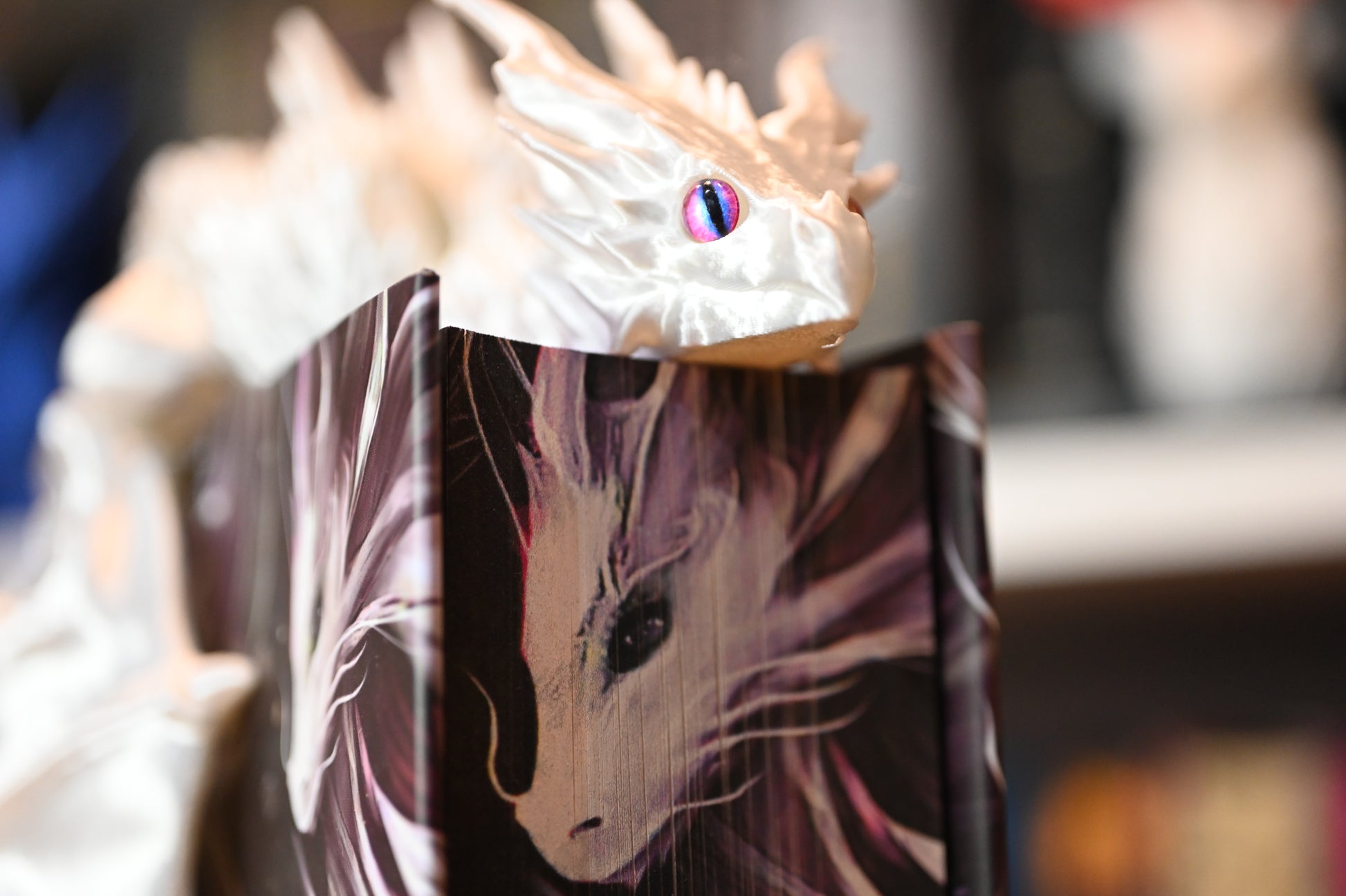 Figurina 3D articulată Dragon alb strălucitor cu ochi violet, așezat pe o carte cu copertă ilustrată, decor fantasy pentru iubitorii de lectură magică.