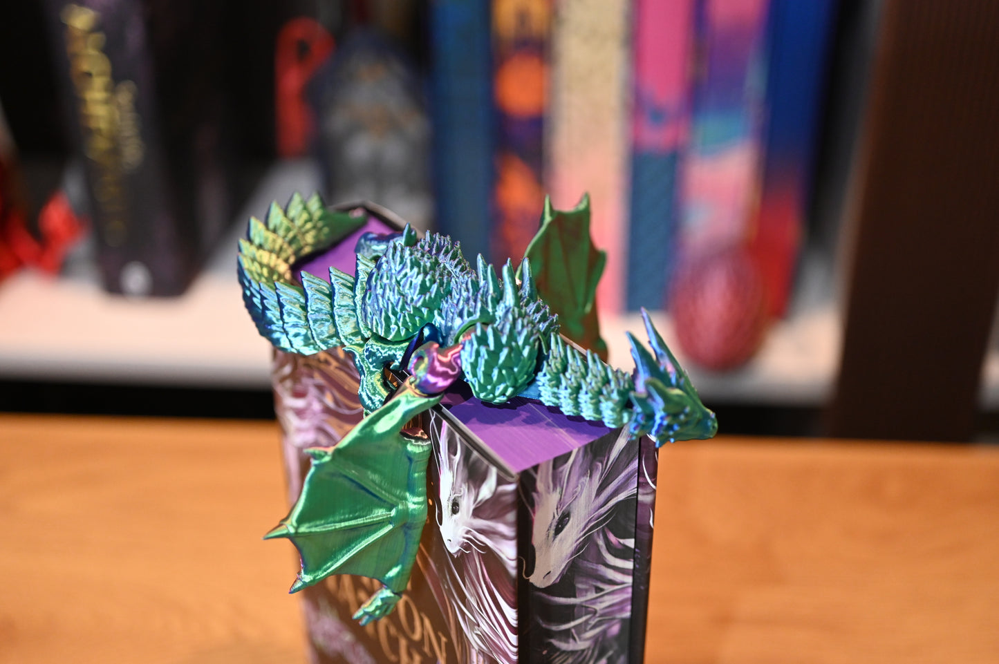 Figurina 3D articulată dragon  iridescent în nuanțe de verde și albastru, cu aripi deschise, așezat pe cartea When the moon hatched, decor de inspirație fantasy