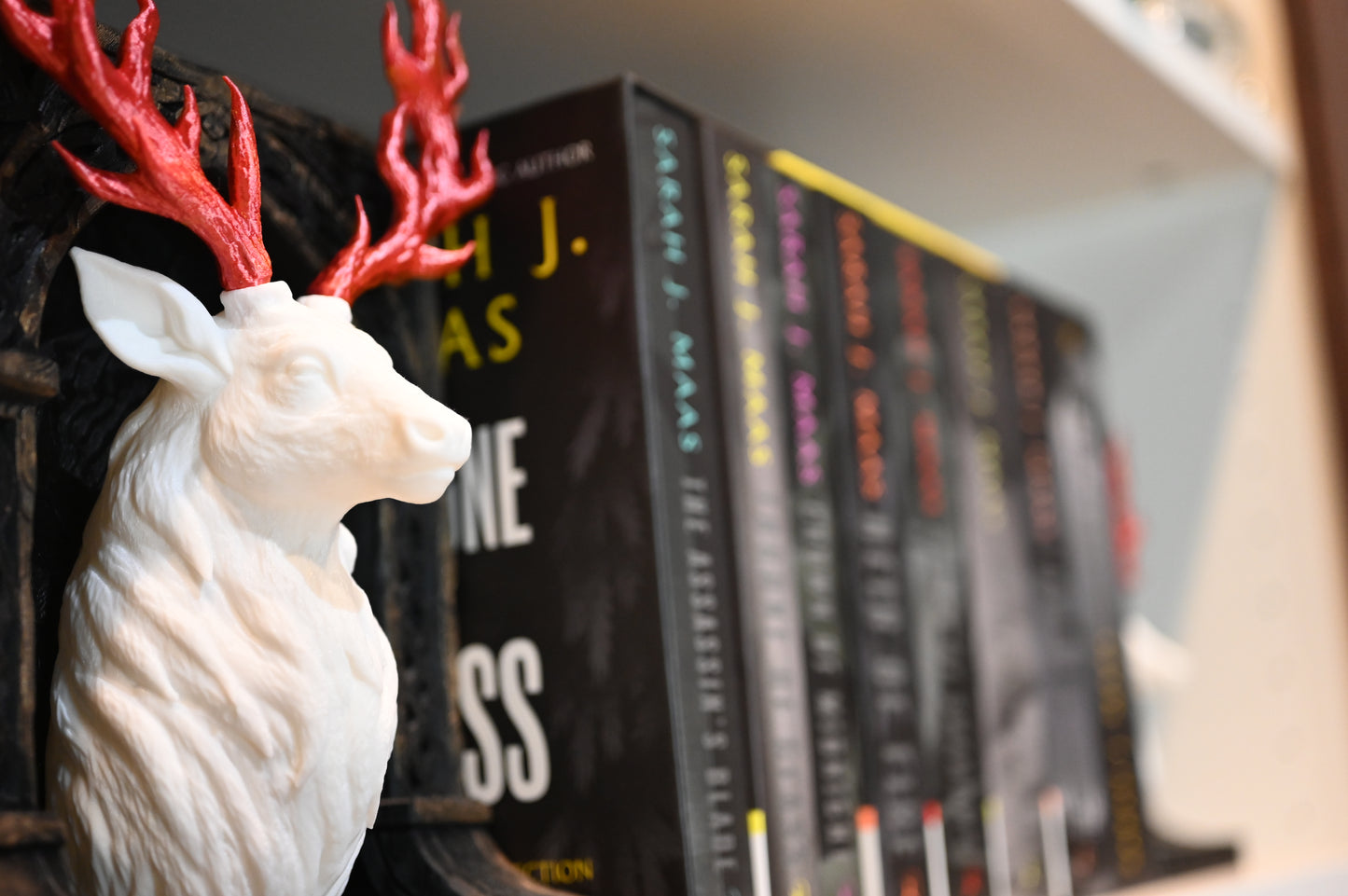 Book nook "Cerbul de jar" cu bust de cerb alb și coarne roșii inflacarate, așezat pe un raft lângă seria Throne of Glass