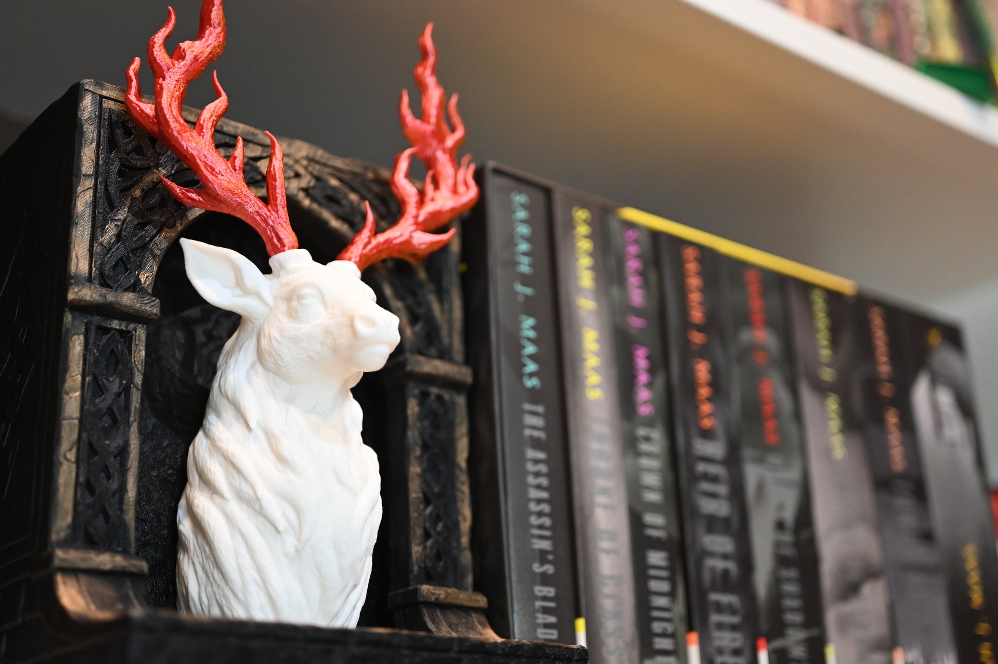 Book nook "Cerbul de jar" cu bust de cerb alb și coarne roșii inflacarate, așezat pe un raft lângă seria Throne of Glass