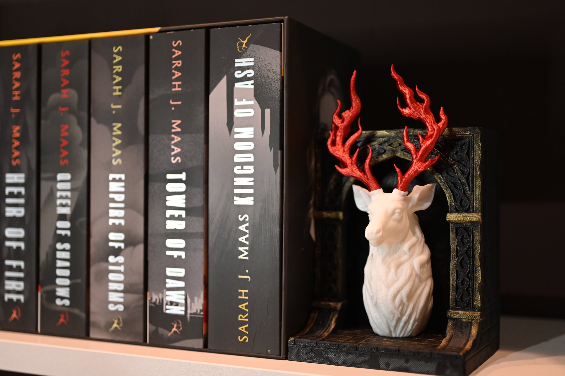 Book nook bust de cerb alb și coarne roșii inflacarate, așezat pe un raft lângă seria Throne of Glass