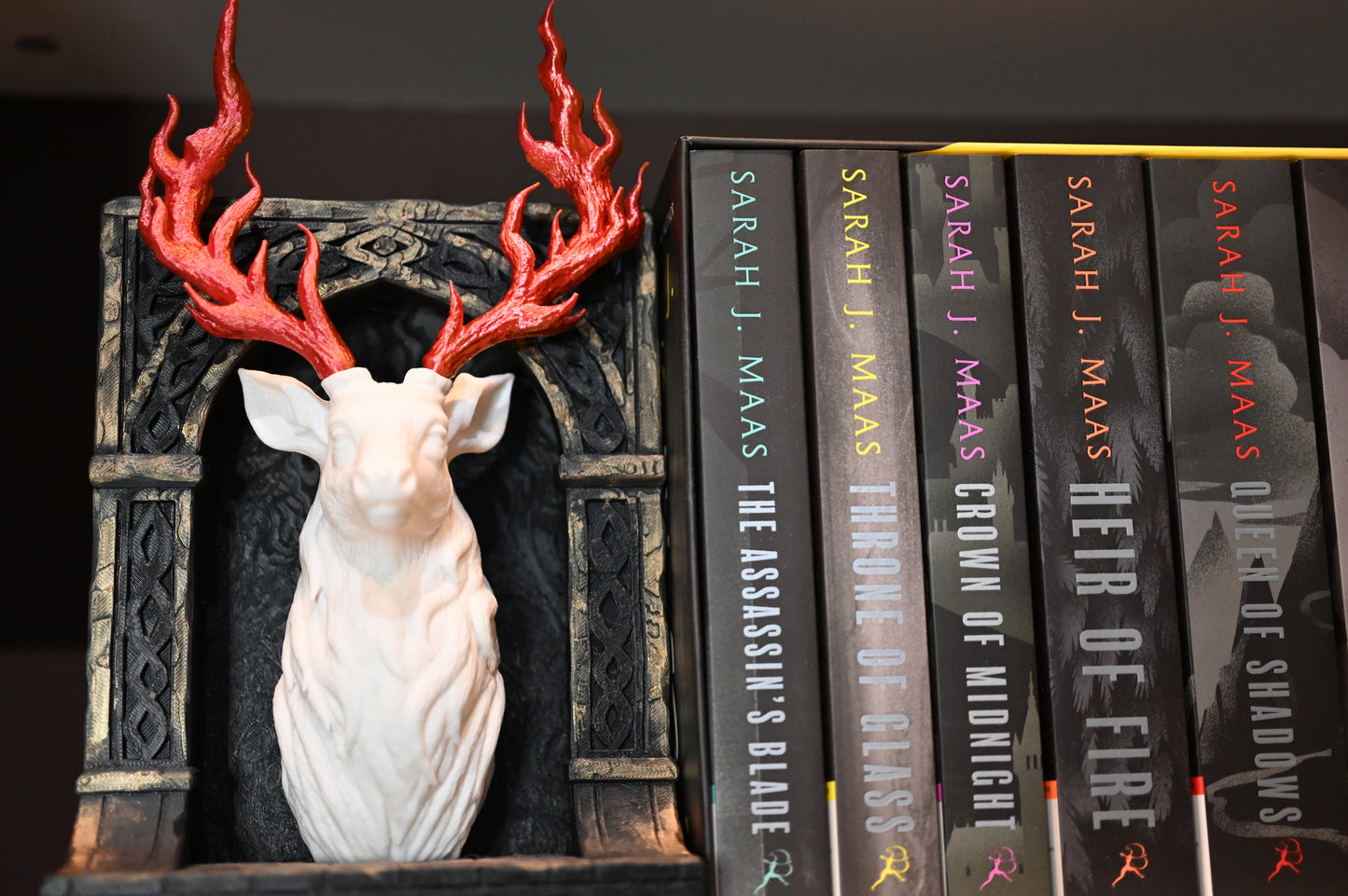 Book nook bust de cerb alb și coarne roșii inflacarate, așezat pe un raft lângă seria Throne of Glass