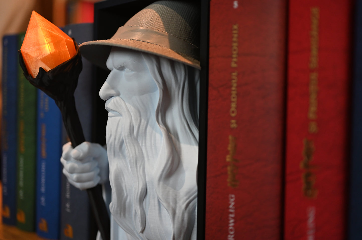 Vrăjitorul Luminii - Book nook Prim-plan al bustului vrăjitorului Gandalf, concentrat pe toiagul său negru cu un cristal portocaliu translucid și detalii ale pălăriei texturate.