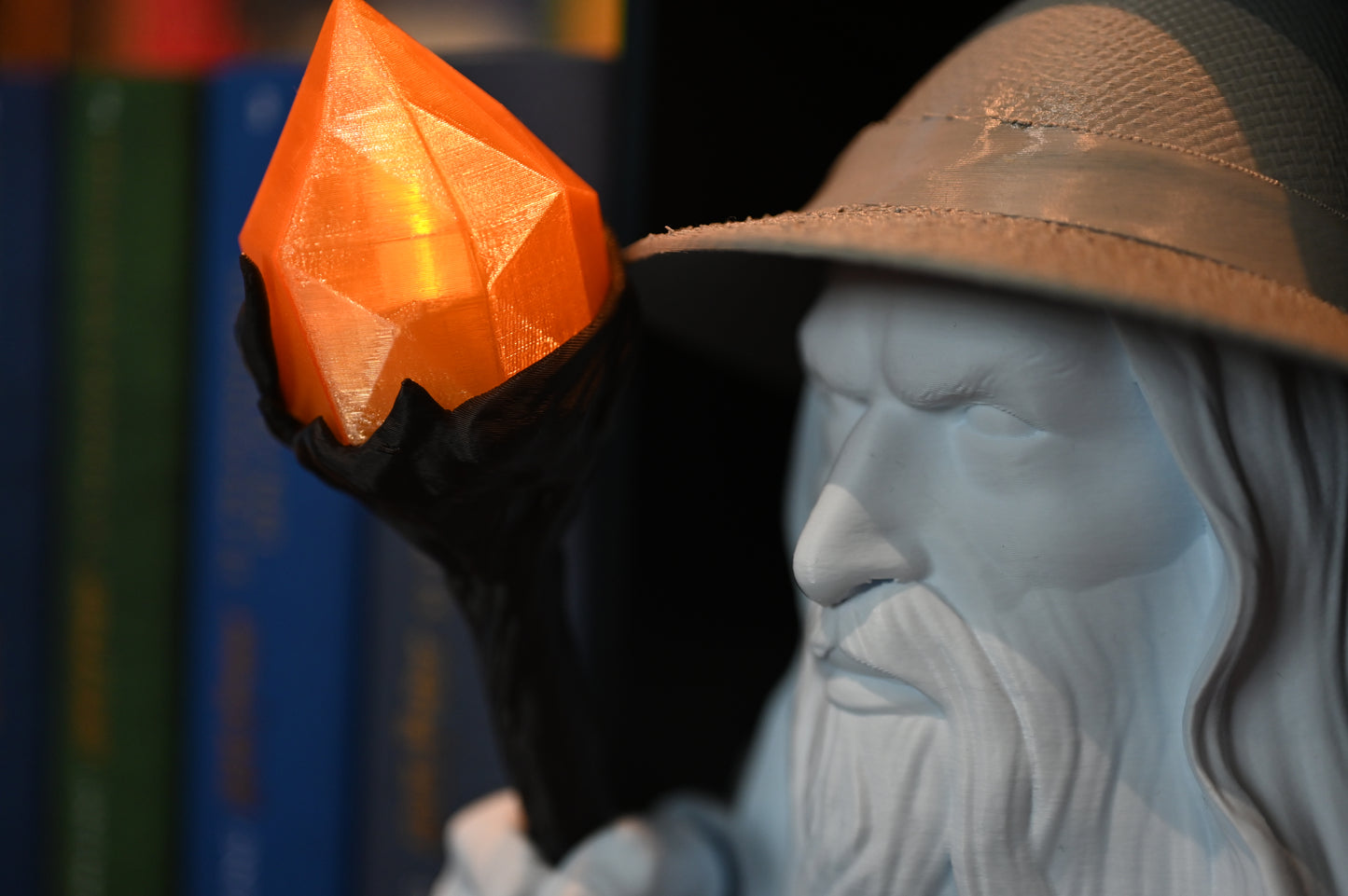 Vrăjitorul Luminii - Book nook Vedere laterală a bustului vrăjitorului între cărți, evidențiind detaliile feței și toiagul cu cristalul portocaliu strălucitor.