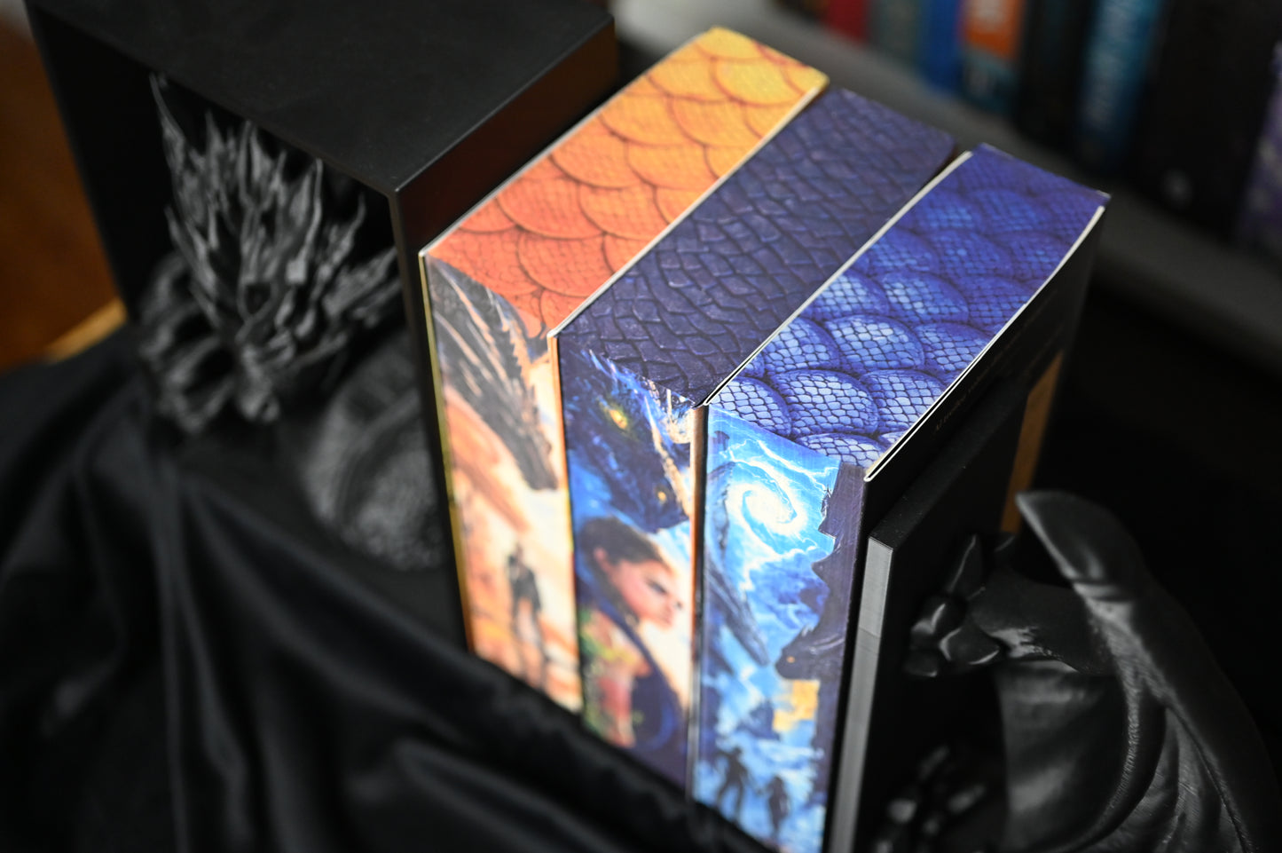 Vedere de sus asupra celor trei volume din seria Empyrean de Rebecca Yarros, cu printed edges personalizate de Printedges. Marginea superioară a fiecărei cărți prezintă modele de solzi în nuanțe portocalii, violet și albastre, simbolizând diferitele legături dintre dragoni și personaje.