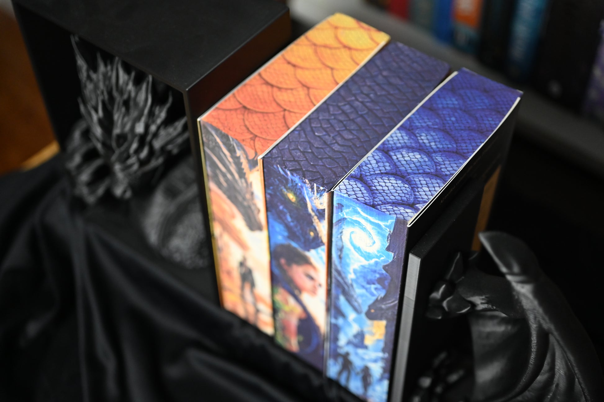 Vedere de sus asupra celor trei volume din seria Empyrean de Rebecca Yarros, cu printed edges personalizate de Printedges. Marginea superioară a fiecărei cărți prezintă modele de solzi în nuanțe portocalii, violet și albastre, simbolizând diferitele legături dintre dragoni și personaje.