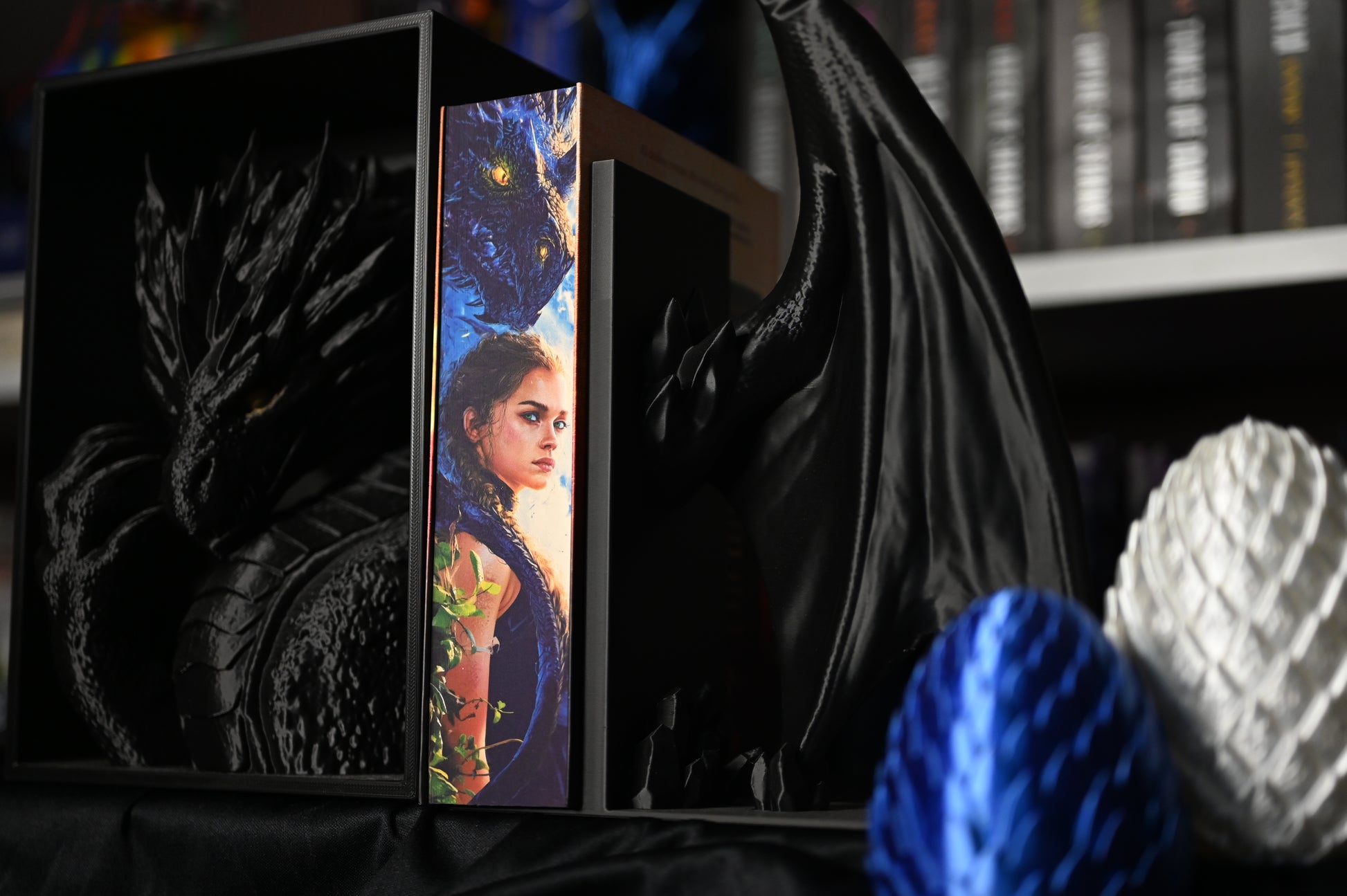 Cartea Flacăra de fier cu printed edges de Rebecca Yarros, ediție specială realizată de Printedges, prezentată între suporturi negre în formă de dragoni. Marginea imprimată (printed edge) arată portretul unei tinere înarmate și capul unui dragon negru cu ochi galbeni, ilustrând perfect universul fantasy al seriei Empyrean.