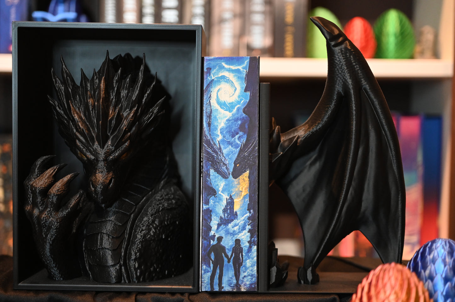 Furtuna de onix cu printed edgesde Rebecca Yarros, ediție specială Printedges, prezentată între suporturi negre în formă de dragoni. Marginea imprimată (printed edge) arată doi dragoni uriași față în față, o furtună magică pe cer și două siluete care se țin de mână în fața unui castel – o scenă fantasy spectaculoasă.