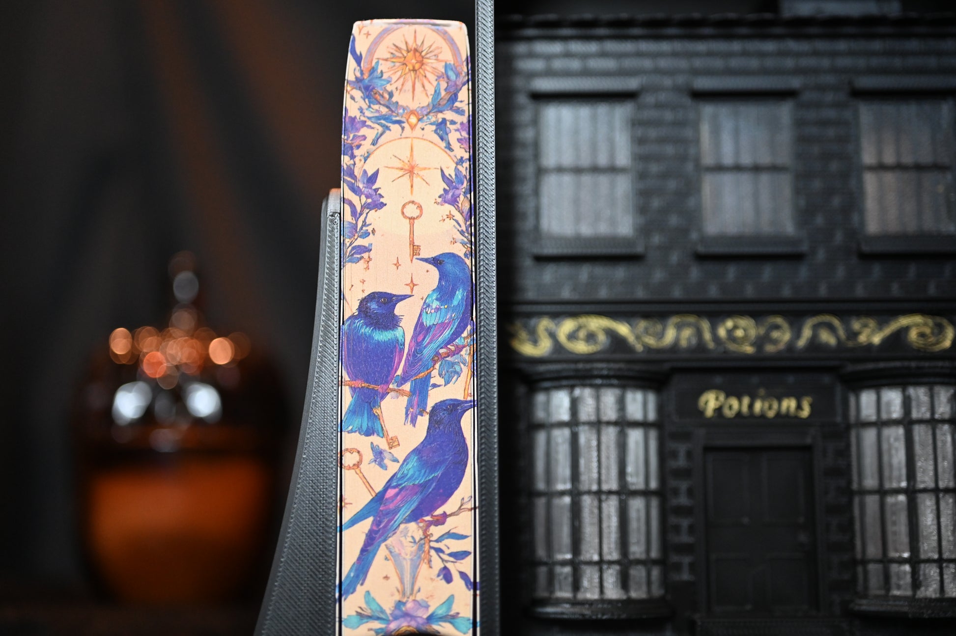 Prim-plan al marginii imprimate a cărții Casa Starling, ilustrând detalii artistice cu păsări și stele aurii pe fundal bej, în stil fantasy.