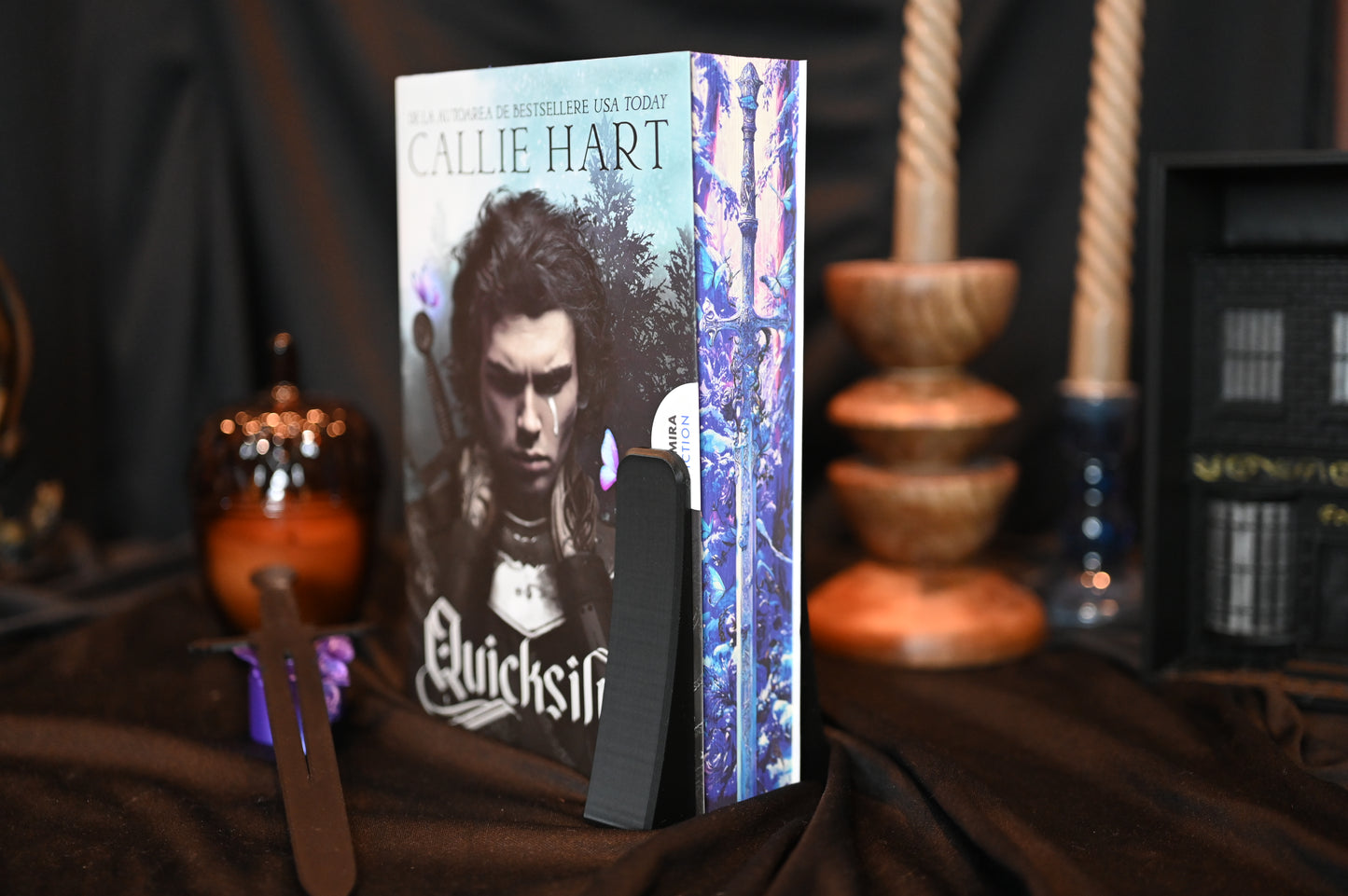 Quicksilver cu printed edges de Callie Hart cu design imprimat pe muchii — sabie argintie, fluturi și elemente magice albastre, expusă într-un decor elegant, pe fundal negru.