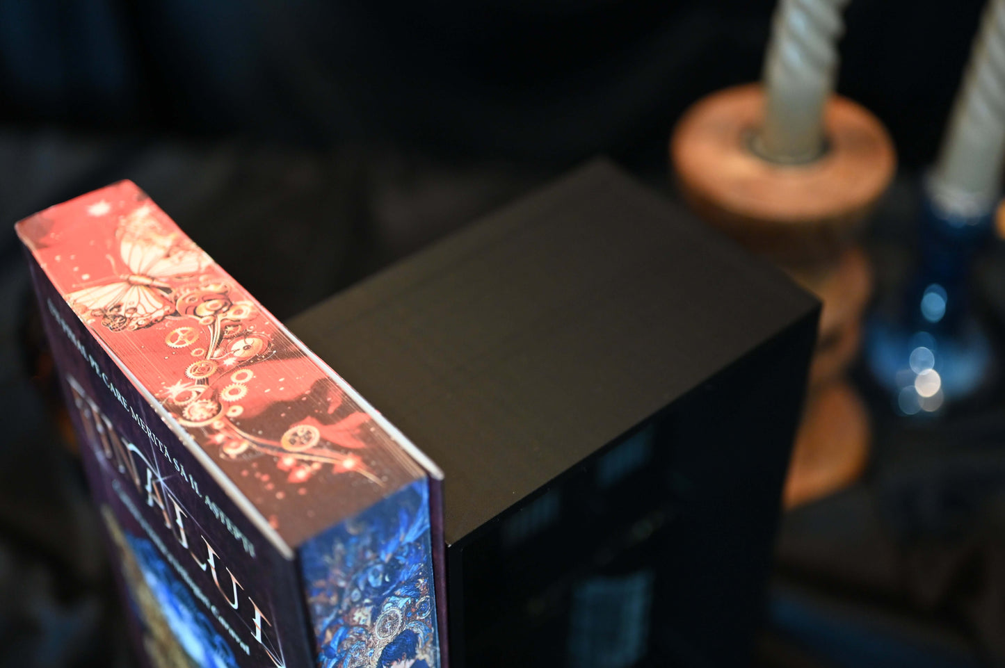 Vedere de sus a cărții "Finalul" cu printed edges, arătând designul imprimat pe muchii cu fluturi și rotițe aurii, în nuanțe de roșu și auriu.