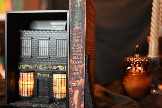 Revrăjită cu printed edges de Lucy Jane Wood, ediție specială cu printed edges. Ilustrația imprimată pe margini prezintă o bibliotecă în nuanțe calde de roșu și portocaliu, cu rafturi pline de cărți și elemente magice ascunse printre ele.