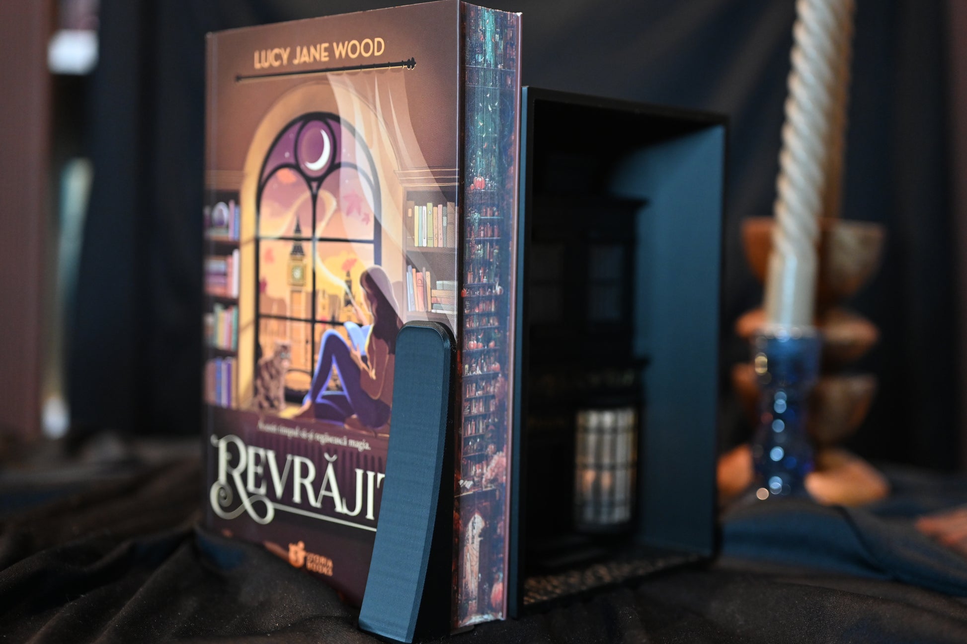 Revrăjită cu printed edges de Lucy Jane Wood, ediție specială cu printed edges. Ilustrația imprimată pe margini prezintă o bibliotecă în nuanțe calde de roșu și portocaliu, cu rafturi pline de cărți și elemente magice ascunse printre ele.