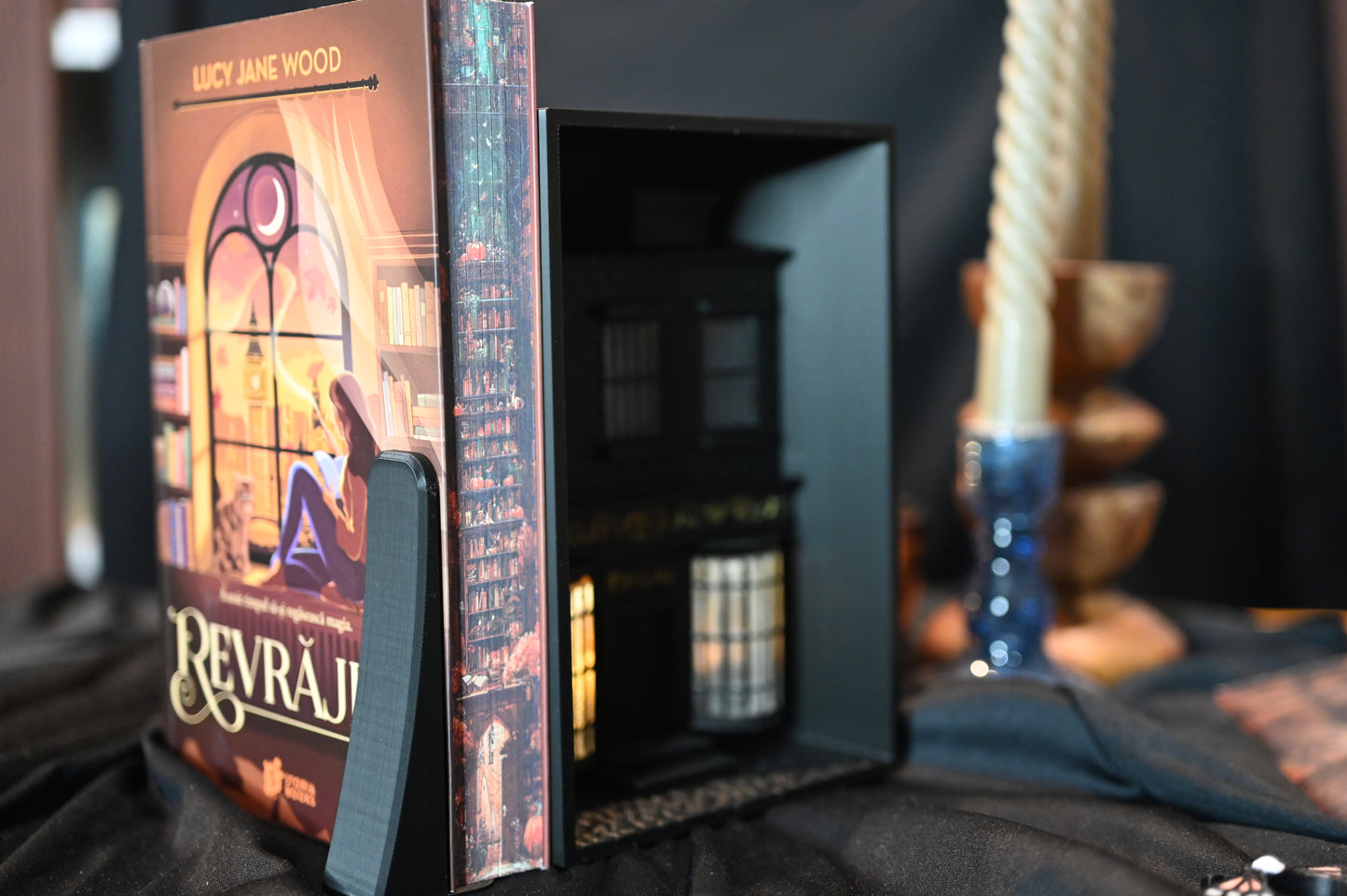 Marginea laterală a cărții Revrăjita de Lucy Jane Wood, ediție specială cu printed edges. Ilustrația imprimată pe margini prezintă o bibliotecă în nuanțe calde de roșu și portocaliu, cu rafturi pline de cărți și elemente magice ascunse printre ele.