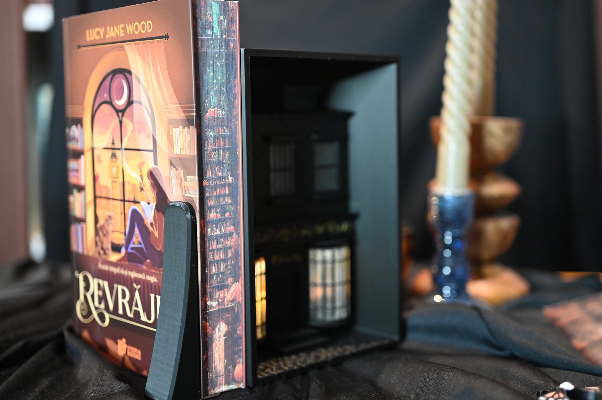 Marginea laterală a cărții Revrăjita de Lucy Jane Wood, ediție specială cu printed edges. Ilustrația imprimată pe margini prezintă o bibliotecă în nuanțe calde de roșu și portocaliu, cu rafturi pline de cărți și elemente magice ascunse printre ele.