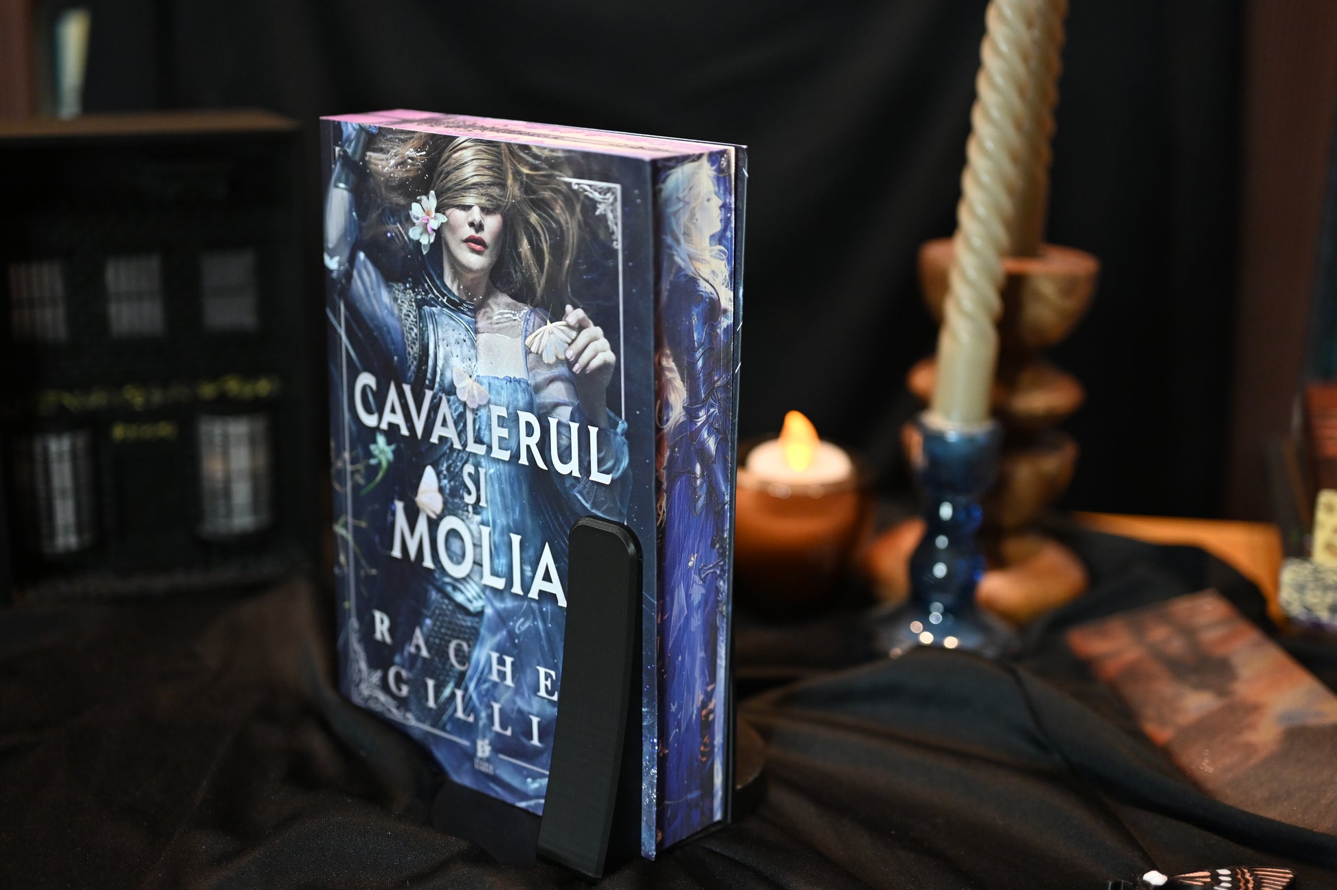 Marginea laterală a cărții Cavalerul și molia cu printed edges de Rachel Gillig, ediție hardcover cu margini ilustrate. Imaginea arată o figură feminină cu păr argintiu și armură albastră, în stil fantasy, imprimată pe latura paginilor.