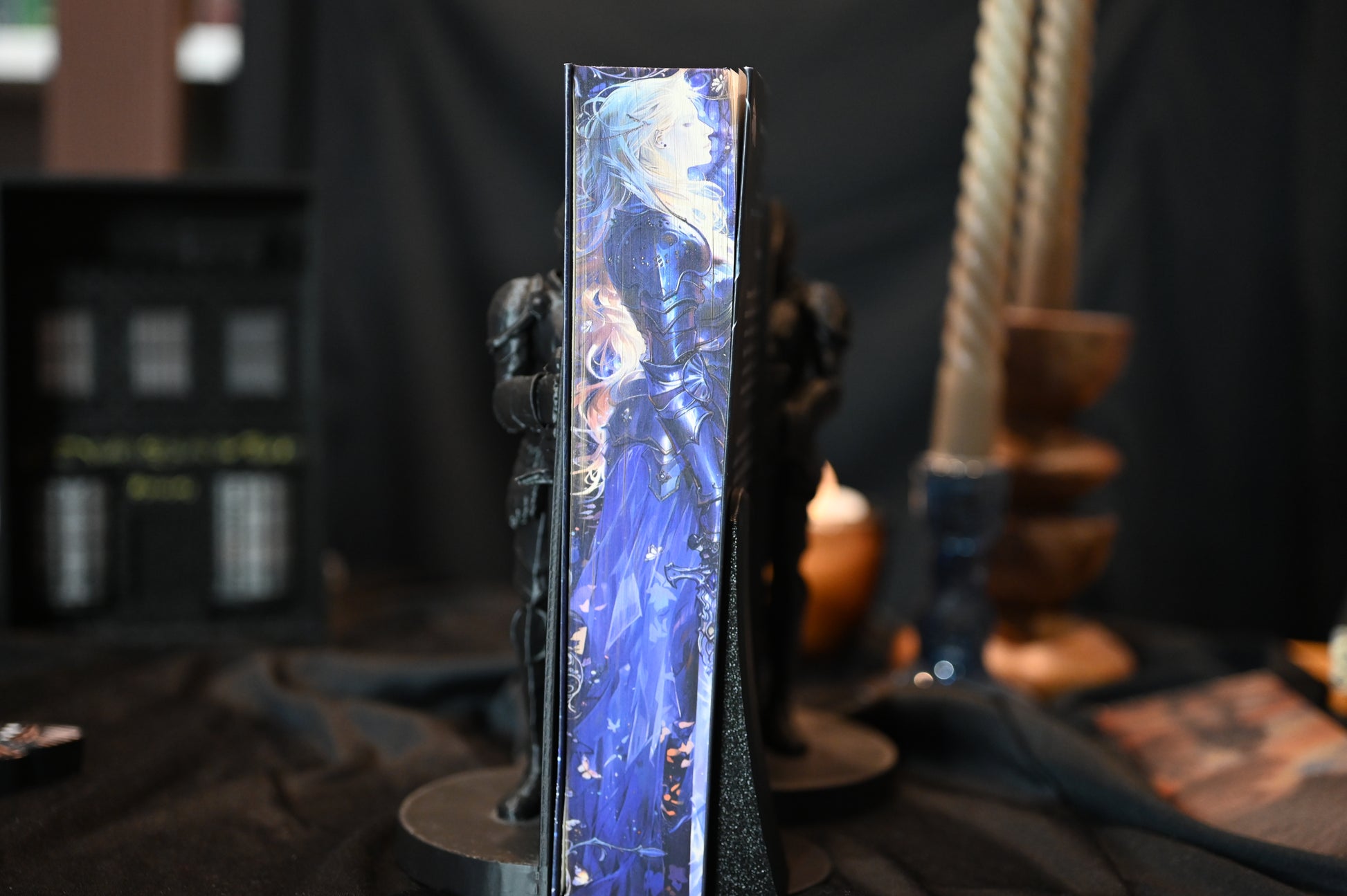 Cartea Cavalerul și Molia de Rachel Gillig, ediție specială cu printed edges. Coperta prezintă o femeie cu părul auriu și ochii acoperiți, iar pe marginea cărții se vede o ilustrație în nuanțe de albastru cu o siluetă în armură