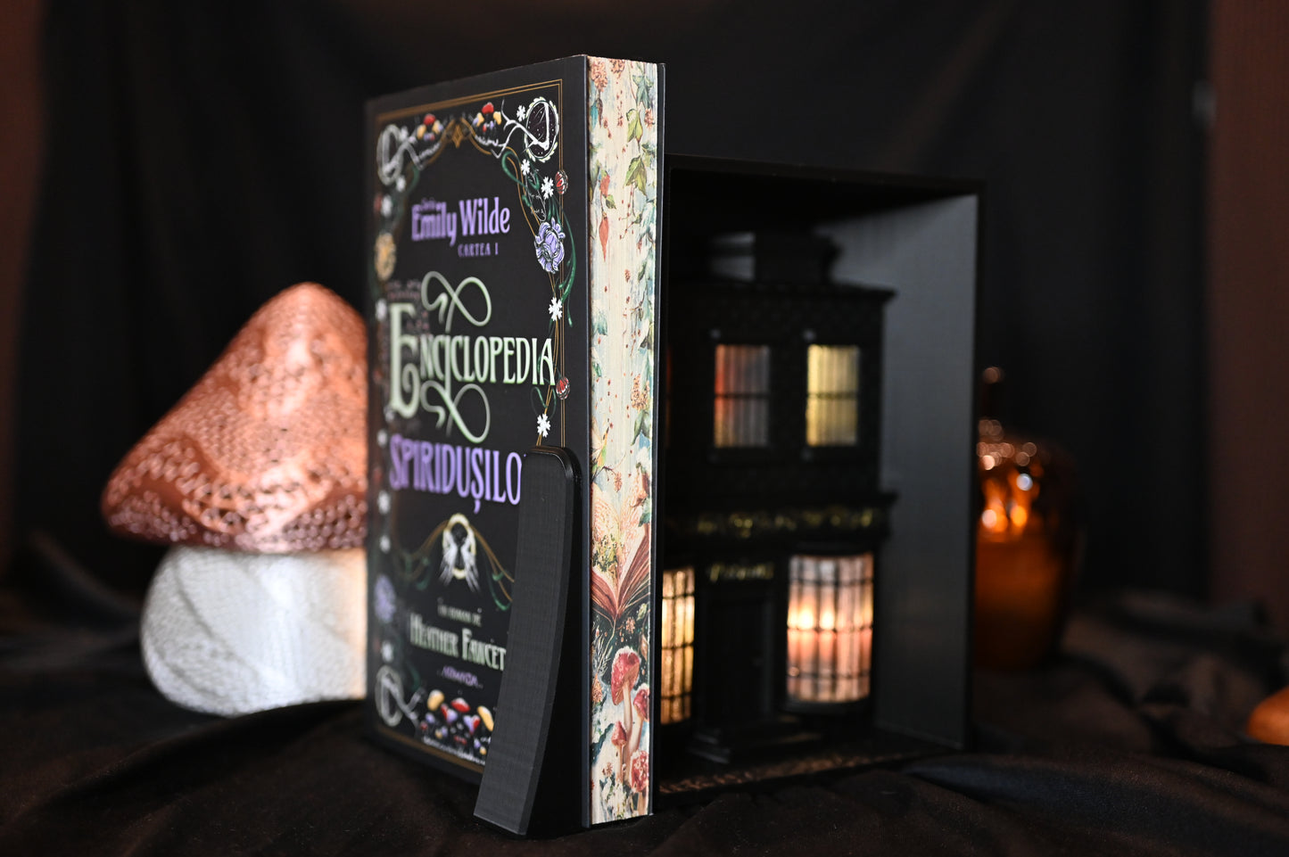 Cartea Enciclopedia spiridușilor de Heather Fawcett, ediție specială cu printed edges. Coperta decorată cu motive florale și titlu în stil victorian, iar marginile paginilor prezintă ilustrații delicate cu ciuperci și flori pe fundal deschis, inspirate din natură.