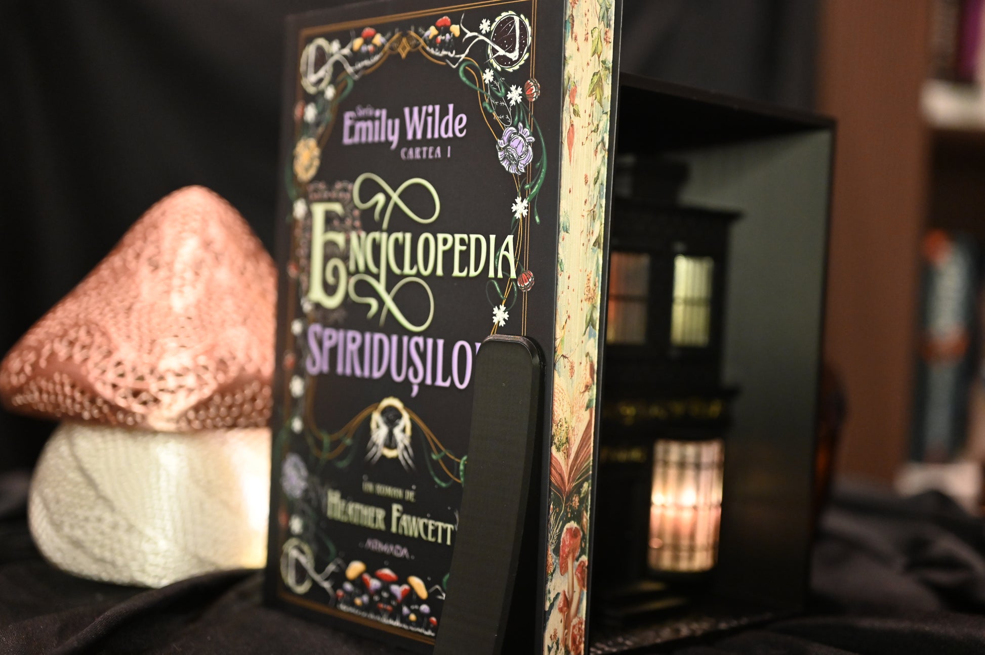 Cartea Enciclopedia spiridușilor de Heather Fawcett, ediție specială cu printed edges. Coperta decorată cu motive florale și titlu în stil victorian, iar marginile paginilor prezintă ilustrații delicate cu ciuperci și flori pe fundal deschis, inspirate din natură.