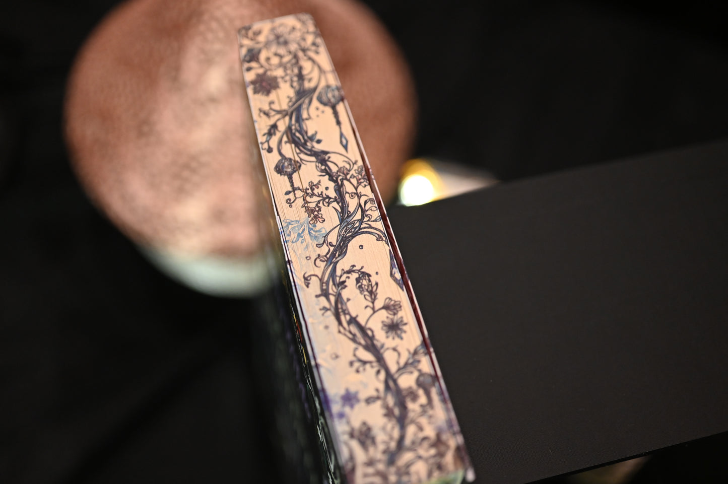 Vedere de sus a cărții Enciclopedia spiridușilor de Heather Fawcett, unde se observă detaliat designul imprimat pe margini: ramuri, frunze și flori desenate în linii fine negre și albastre, pe un fundal crem vintage.