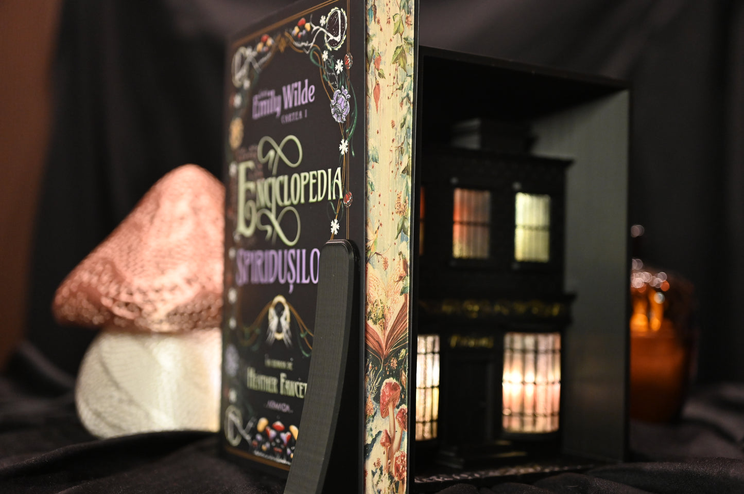 Cartea Enciclopedia spiridușilor de Heather Fawcett, ediție specială cu margini ilustrate. Coperta decorată cu motive florale și titlu în stil victorian, iar marginile paginilor prezintă ilustrații delicate cu ciuperci și flori pe fundal deschis, inspirate din natură.