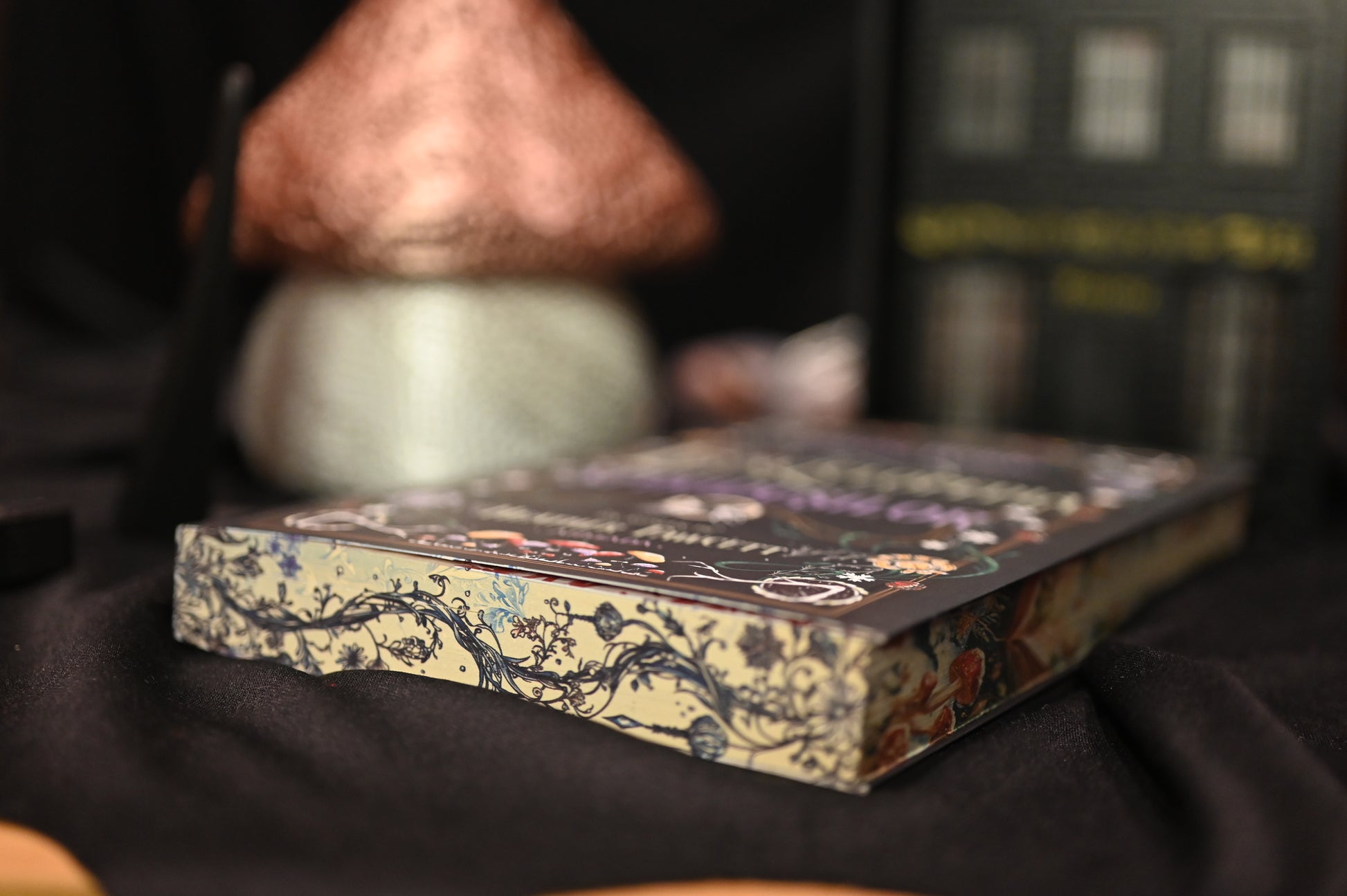 Cartea Enciclopedia spiridușilor de Heather Fawcett, fotografiată în poziție orizontală, evidențiind marginea laterală cu ilustrații botanice și elemente magice — liane, ciuperci și flori — într-un stil artistic de basm.