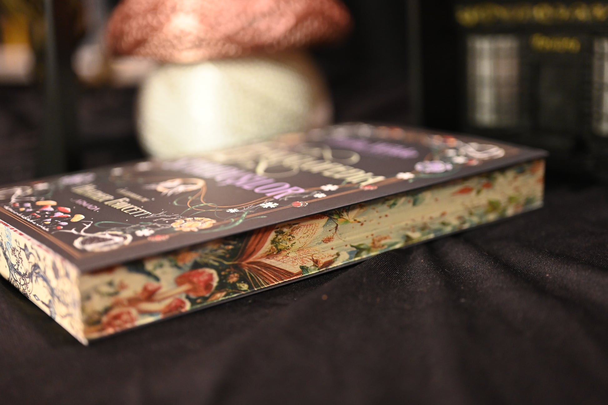 Cartea Enciclopedia spiridușilor de Heather Fawcett, fotografiată în poziție orizontală, evidențiind marginea laterală cu ilustrații botanice și elemente magice — liane, ciuperci și flori — într-un stil artistic de basm.