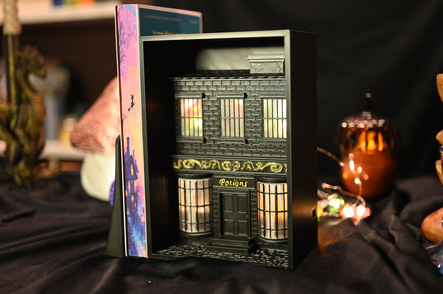 Cartea Societatea secretă a vrăjitoarelor de Sangu Mandanna, ediție specială cu margini ilustrate (printed edges). Marginea laterală a paginilor prezintă o casă iluminată sub cer roz-auriu, cu silueta unei vrăjitoare zburând pe mătură, în stil ilustrat magic.