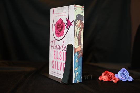 Flawless cu printed edges  de Elsie Silver, ediție cu margini imprimate, design cu trandafir roz și pereche de cowboy, expusă pe un suport negru decorativ.