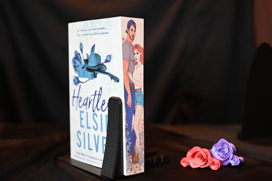 Cartea Heartless cu printed edges de Elsie Silver, ediție cu margini imprimate, în nuanțe de albastru, prezentată pe un fundal negru cu trandafiri decorativi