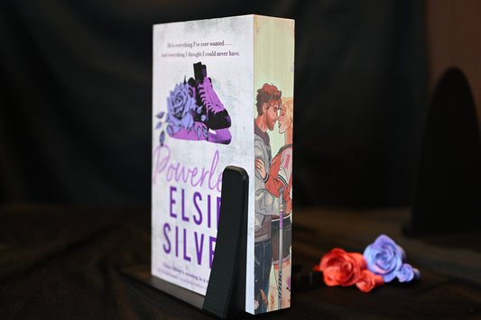 Cartea Powerless cu printed edges de Elsie Silver, ediție cu margini imprimate violet, arată un cuplu romantic: un tânăr în hanorac gri ținând în brațe o fată blondă îmbrăcată sport, cu un pulover de hochei. Marginea prezintă o ilustrație cu o patină violet și trandafiri 