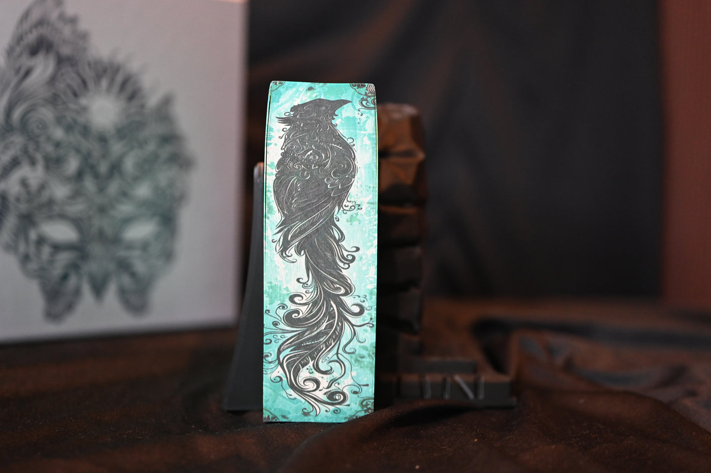 Detaliu al marginii imprimate a volumului A Court of Mist and Fury, cu ilustrația unui corb stilizat pe fundal turcoaz.