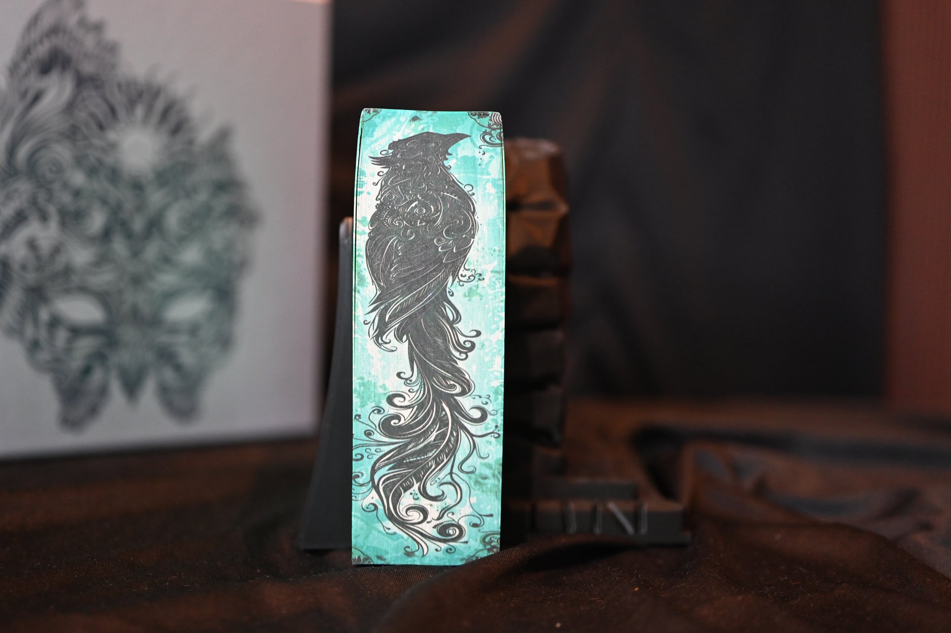 Detaliu al marginii imprimate a volumului A Court of Mist and Fury, cu ilustrația unui corb stilizat pe fundal turcoaz.