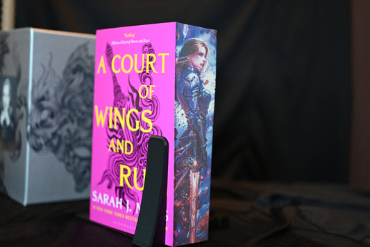 Set Acotar cu printed edges Cartea A Court of Wings and Ruin cu copertă fucsia și margini imprimate ce prezintă o femeie războinică în armură și o sabie magică.