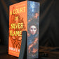 Cartea A Court of Silver Flames cu printed edges de Sarah J. Maas, cu copertă portocalie și margini imprimate ce prezintă portretul unei femei elfice învăluită în flăcări argintii.