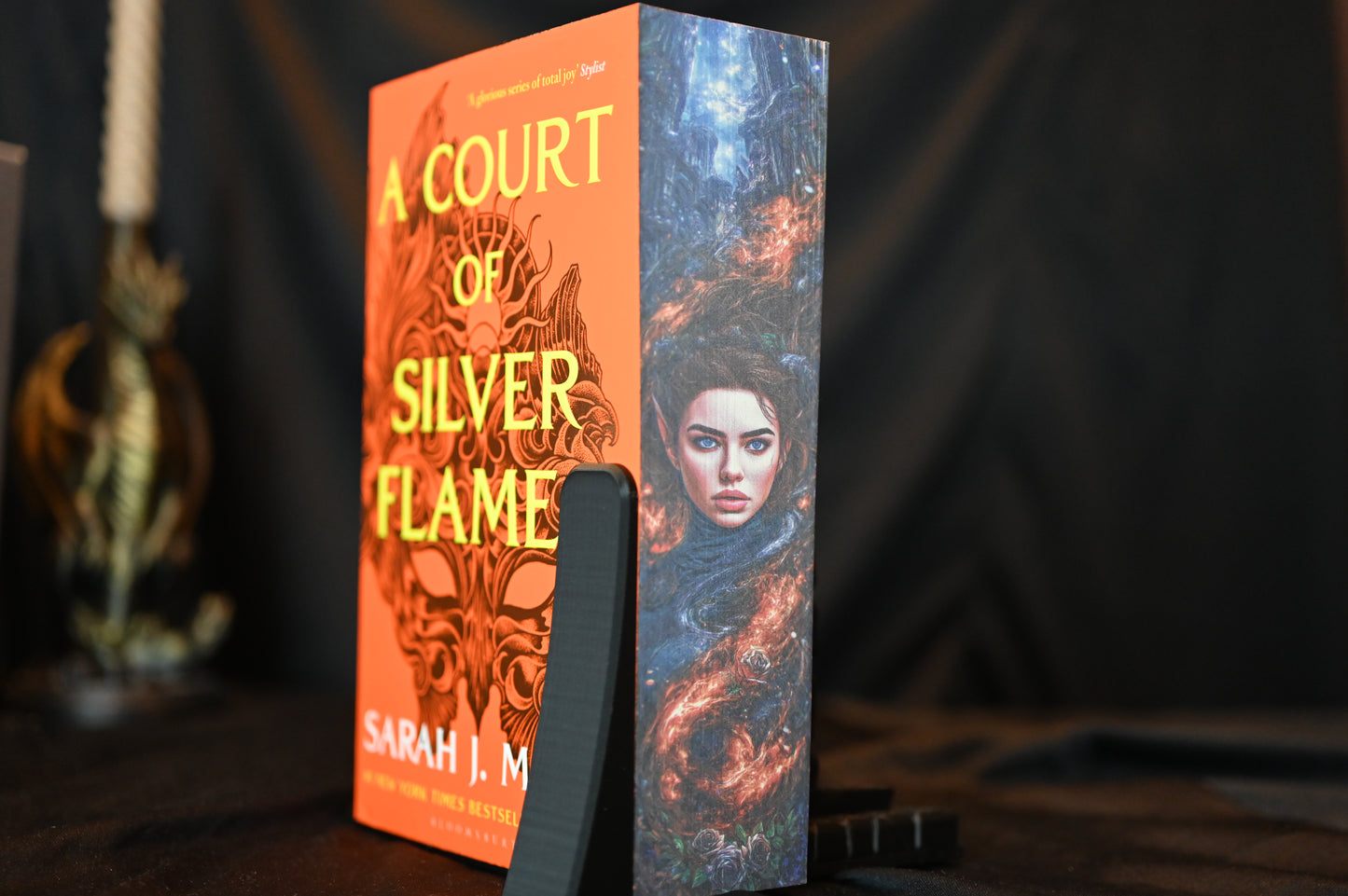 Cartea A Court of Silver Flames cu printed edges de Sarah J. Maas, cu copertă portocalie și margini imprimate ce prezintă portretul unei femei elfice învăluită în flăcări argintii.