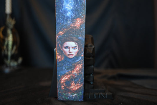 Cartea A Court of Silver Flames cu printed edges de Sarah J. Maas, cu copertă portocalie și margini imprimate ce prezintă portretul unei femei elfice învăluită în flăcări argintii.