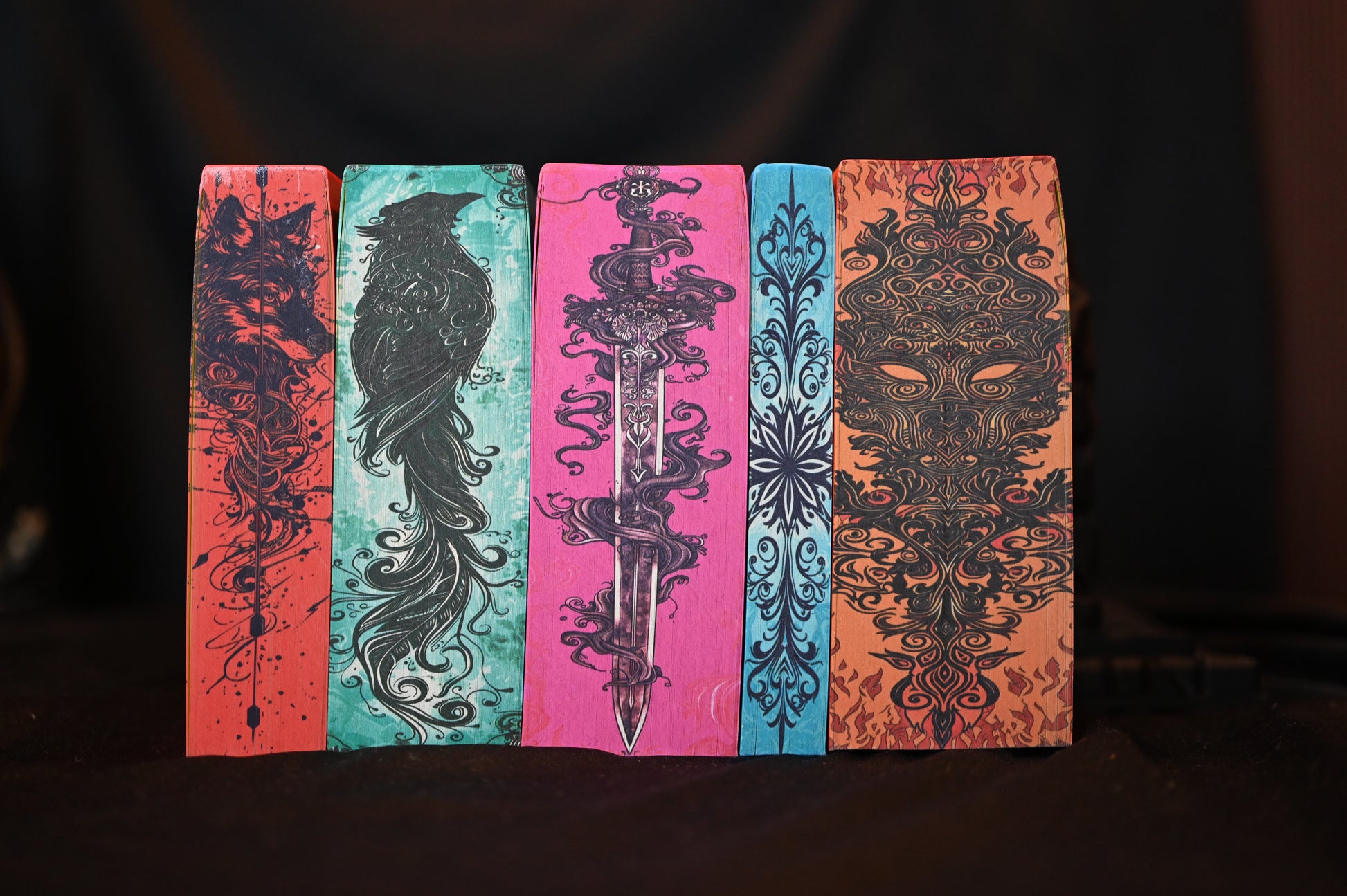 Set ACOTAR cu printed edges – cinci volume cu margini ilustrate artistic: lup, corb, sabie, motiv floral și mască de foc.