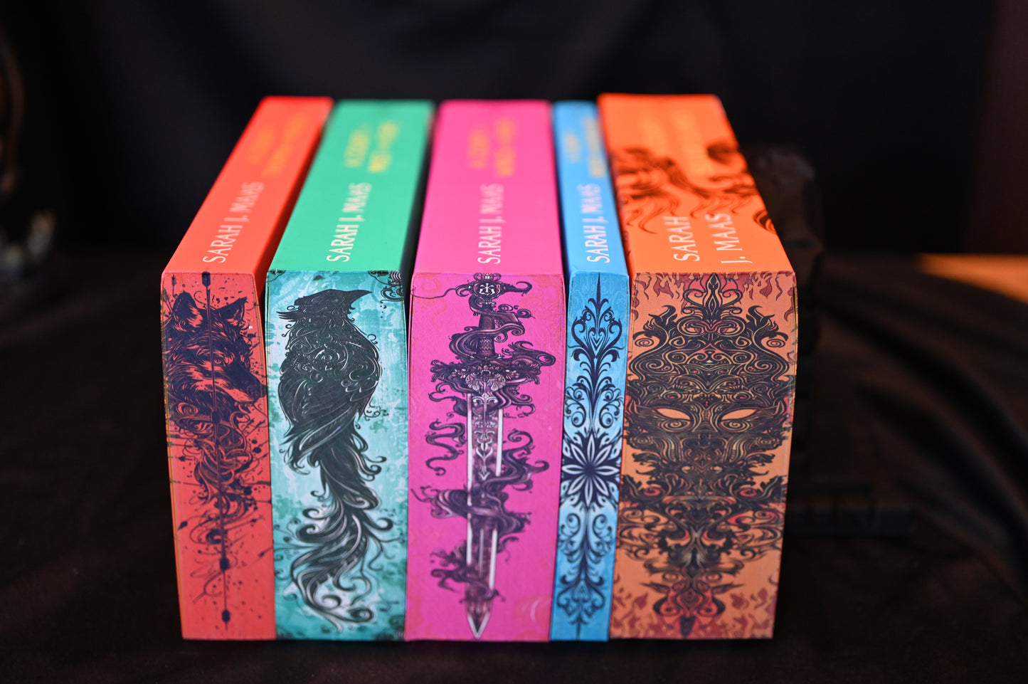 Set ACOTAR cu printed edges – cinci volume cu margini ilustrate artistic: lup, corb, sabie, motiv floral și mască de foc.