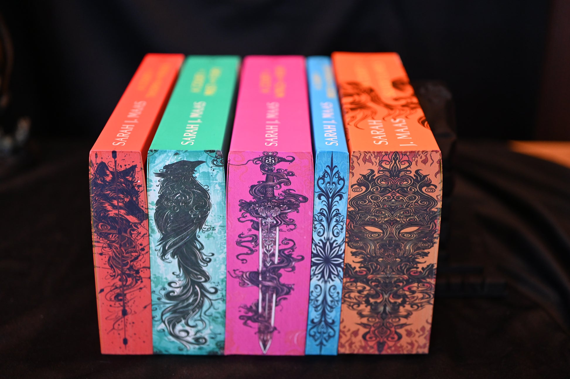 Set ACOTAR cu printed edges – cinci volume cu margini ilustrate artistic: lup, corb, sabie, motiv floral și mască de foc.