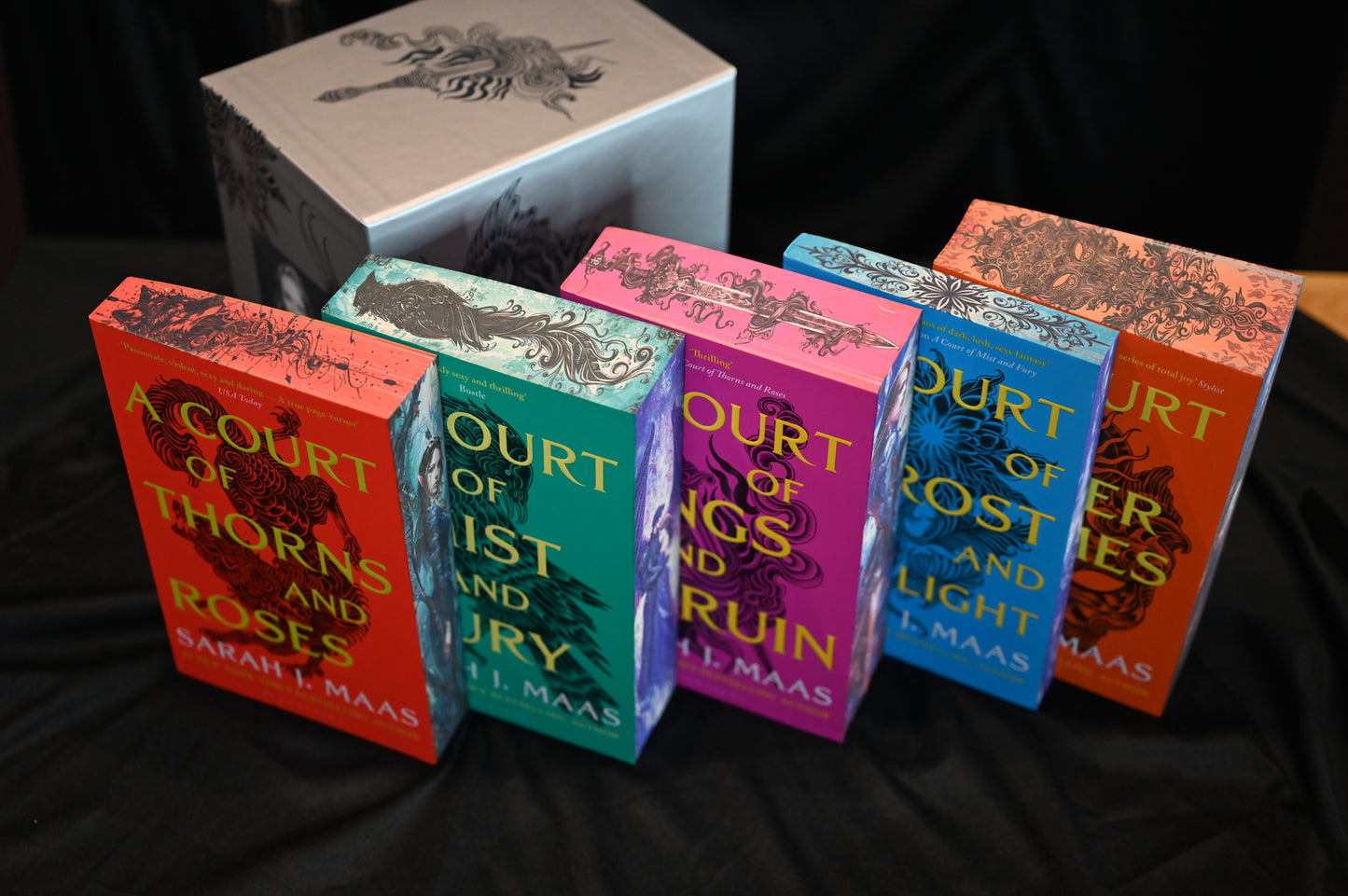 Setul de cărți A Court of Thorns and Roses de Sarah J. Maas cu margini imprimate colorate, expuse alături de cutia decorată ACOTAR.