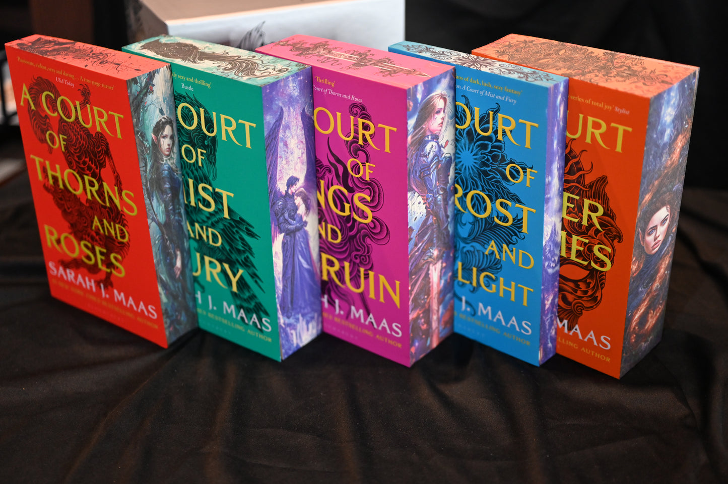 Setul de cărți A Court of Thorns and Roses de Sarah J. Maas cu margini imprimate colorate, expuse alături de cutia decorată ACOTAR.