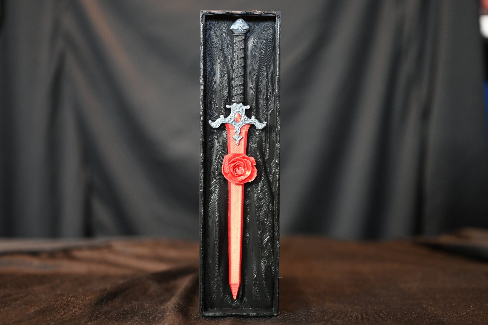 Book nook „The Hidden Rose Sword” – sabie roșie cu trandafir sculptat, așezată într-o cutie decorativă neagră cu textură gotică.