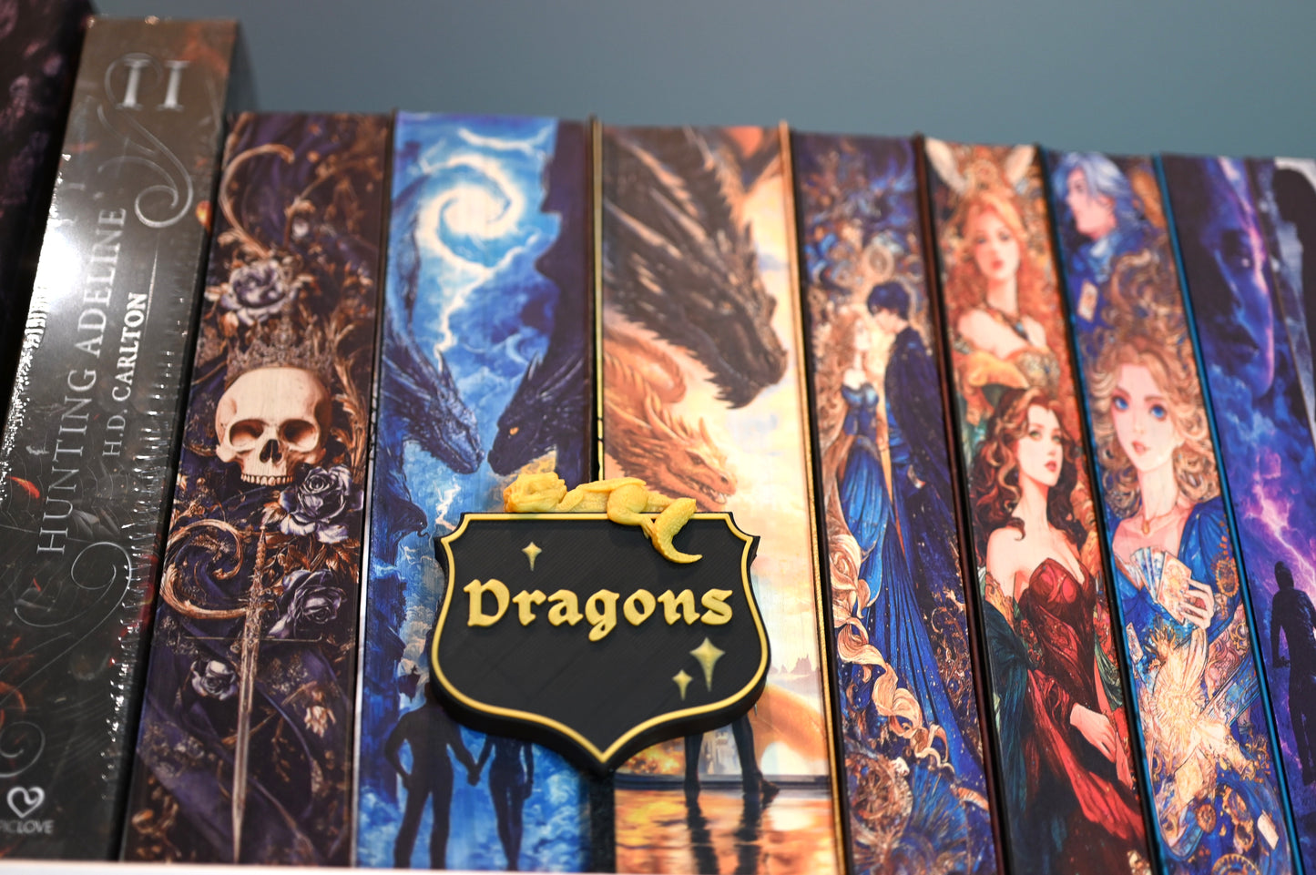 Etichetă 3D pentru secțiunea Dragons, în stil heraldic negru cu bordură aurie, decorată cu un mic dragon galben care stă întins deasupra.