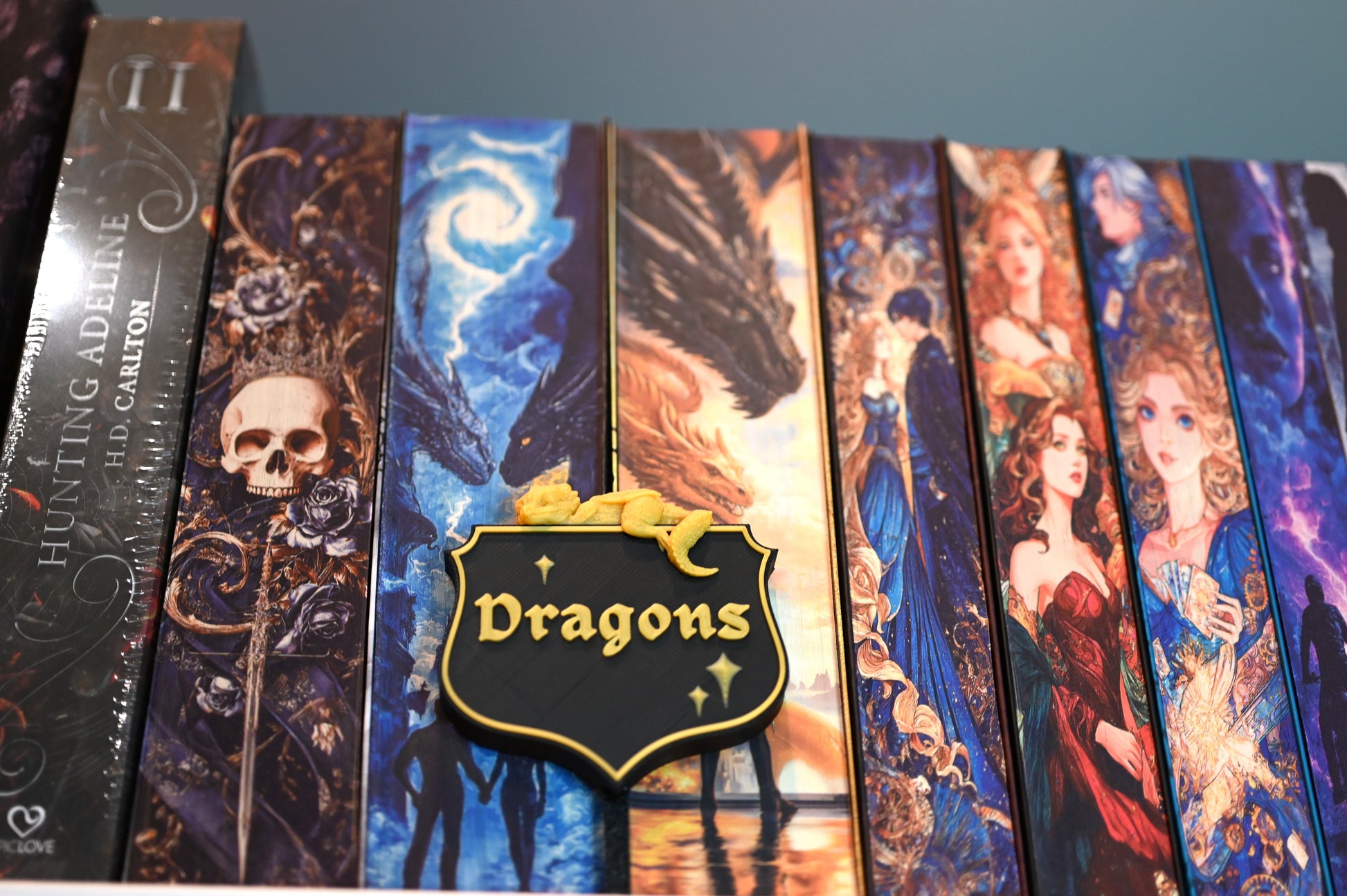 Etichetă 3D pentru secțiunea Dragons, în stil heraldic negru cu bordură aurie, decorată cu un mic dragon galben care stă întins deasupra.