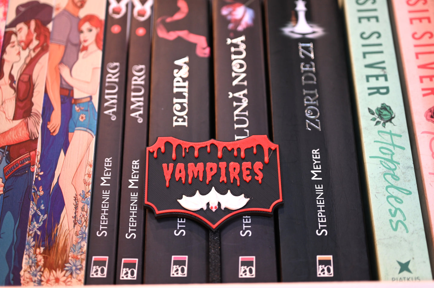 Etichetă 3D Vampires, neagră cu margini roșii, litere roșii care par scurse și un liliac alb cu ochi roșii în partea de jos.