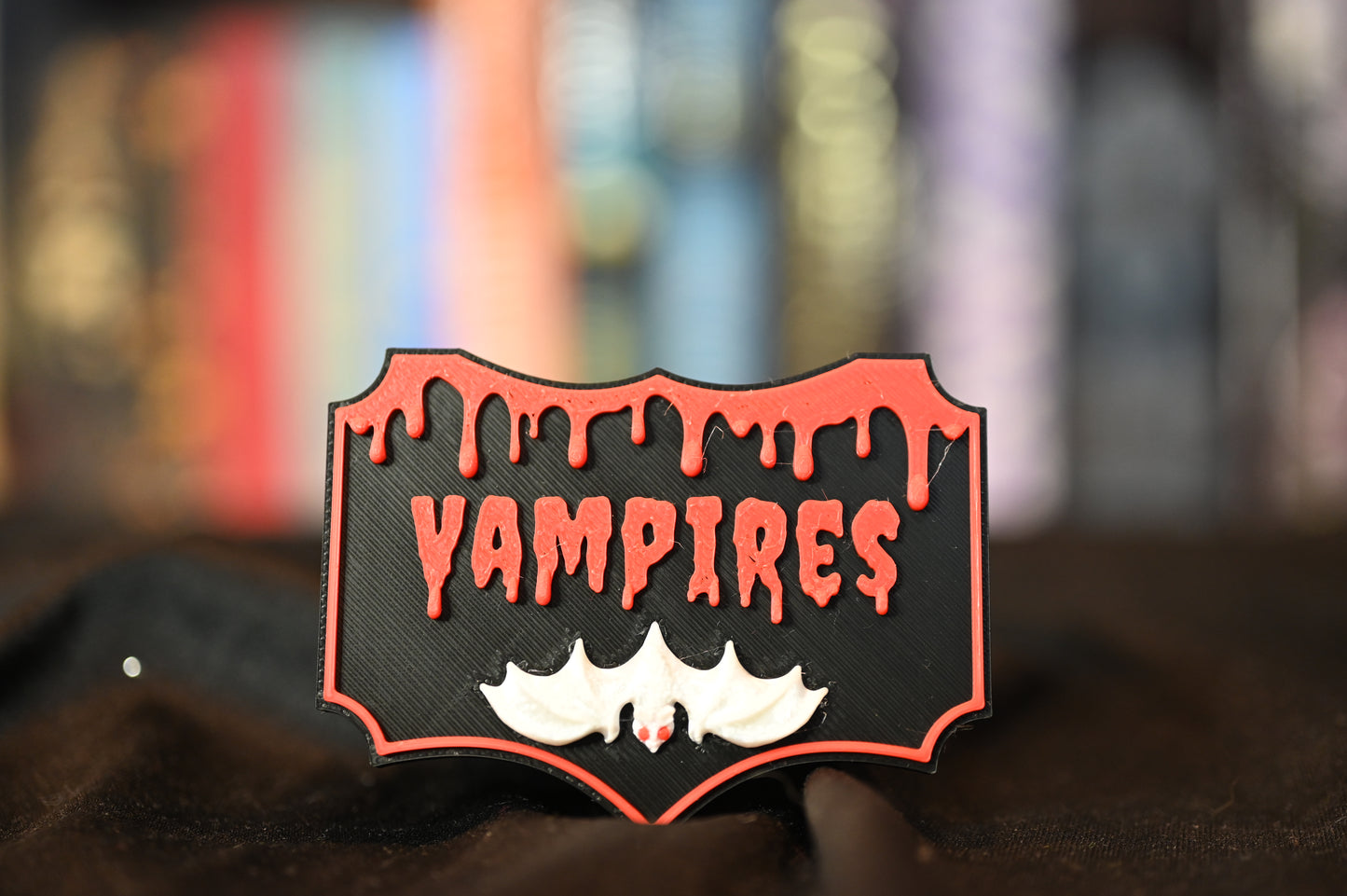 Etichetă 3D Vampires, neagră cu detalii roșii ca sângele și un liliac alb, compatibilă cu două moduri de fixare: agățare pe poliță sau prindere autoadezivă